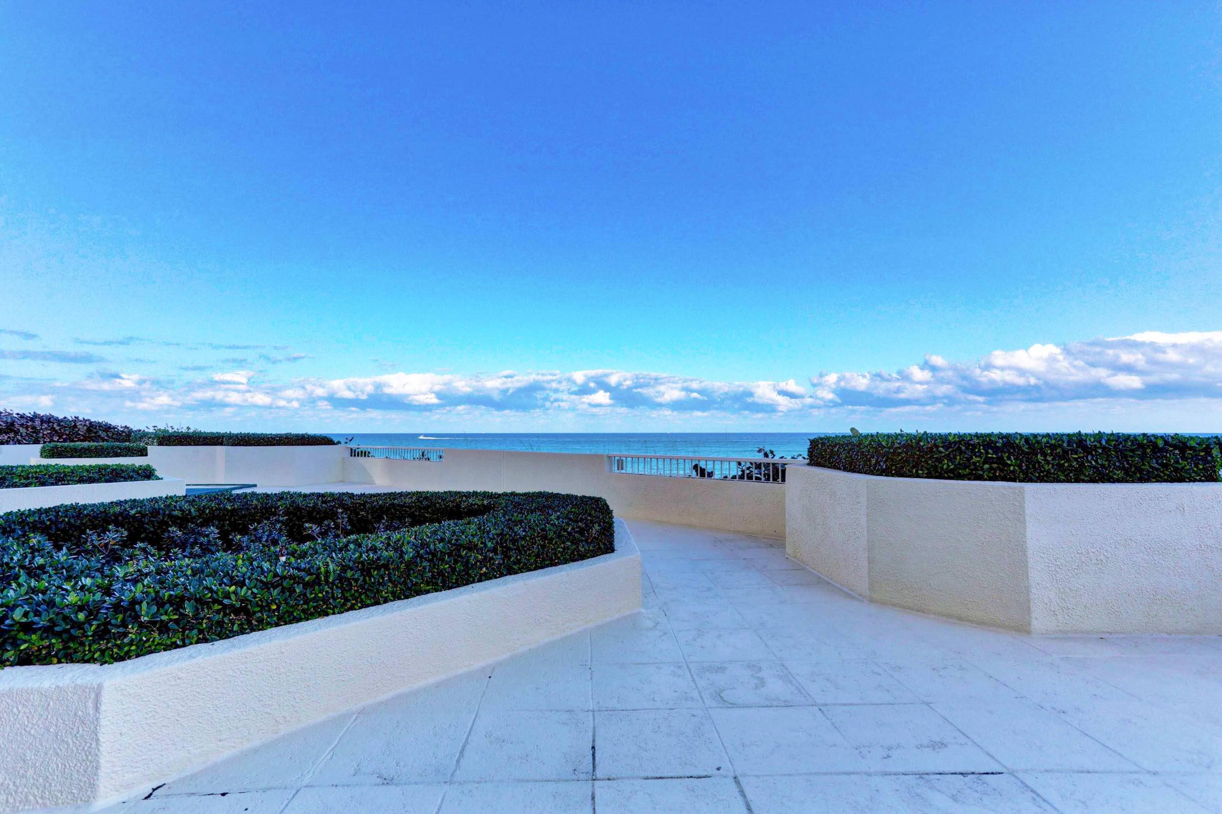 Oceanfront terrace with tiled paving, raised hedges, and a wide ocean view.