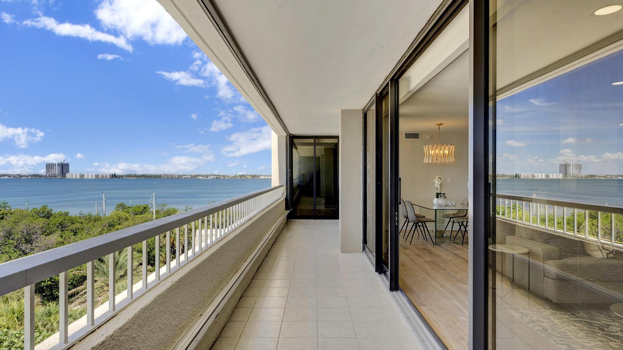 Apartment balcony overlooking blue water, with a dining area visible through the sliding glass doors.