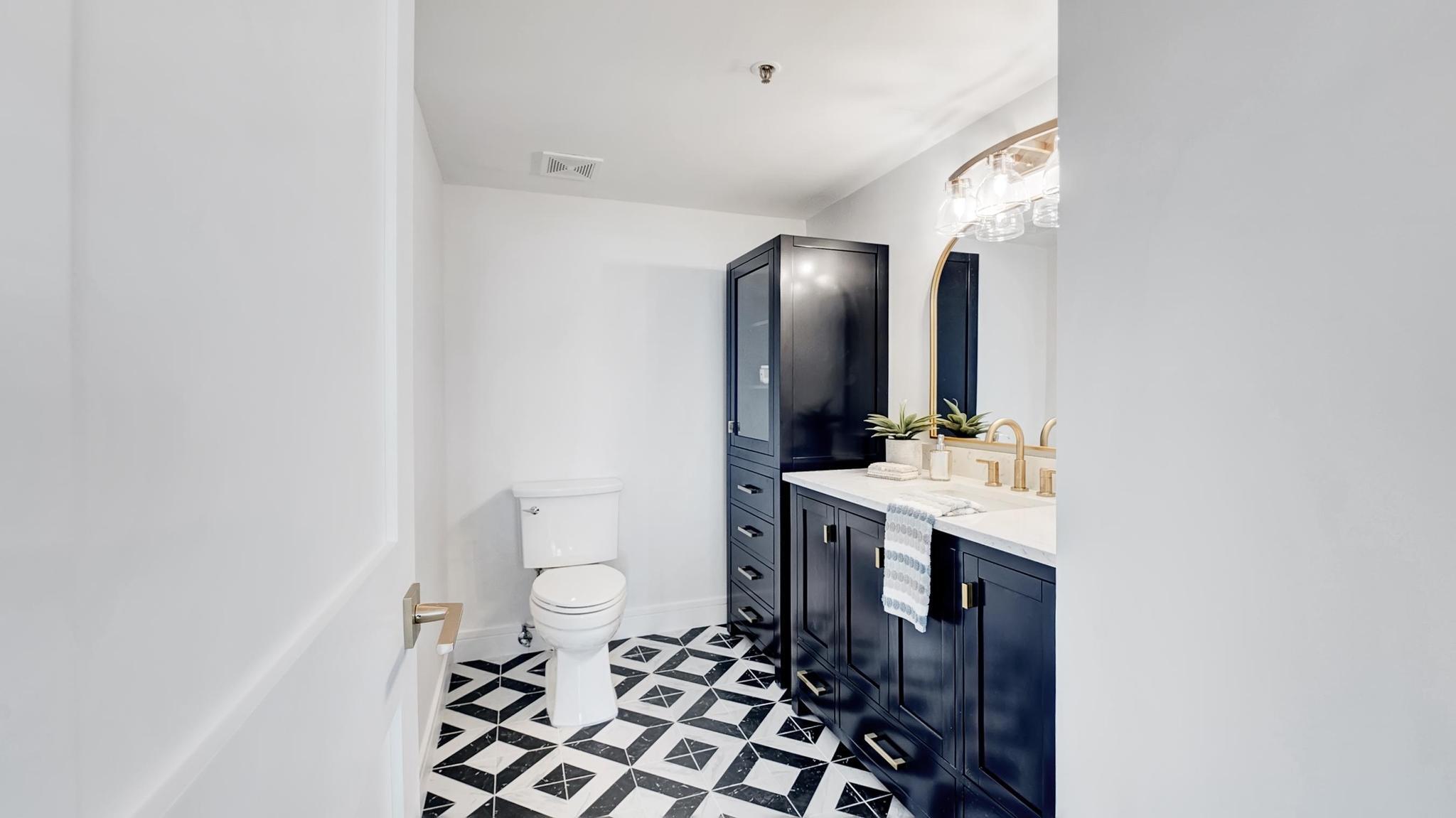 Bathroom with navy vanity, brass fixtures, arched mirror, and black-and-white geometric tile floor.