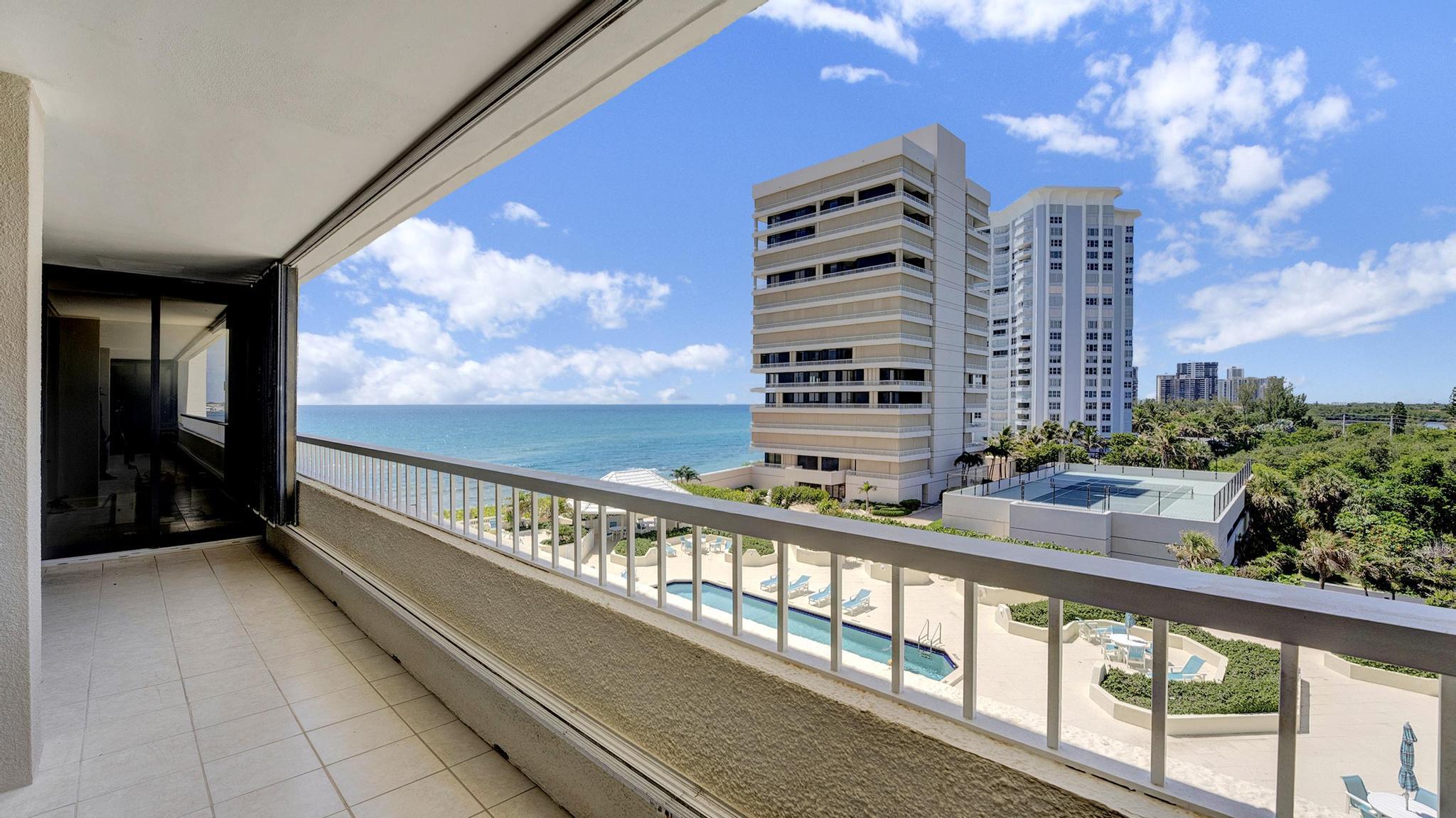 Condominium balcony overlooking the ocean, with a pool deck and tennis court below.