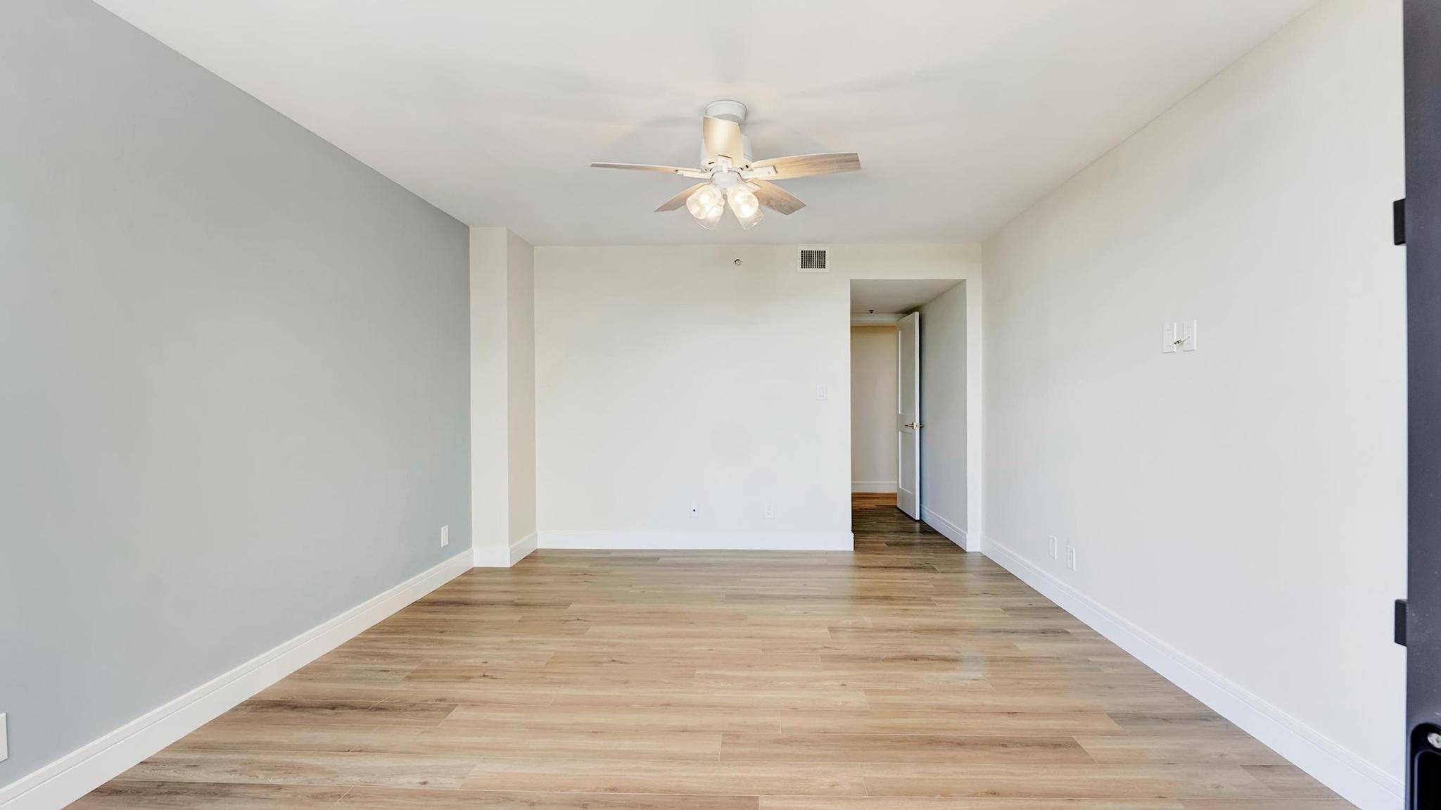 Empty living room with wood-look tile floors and a ceiling fan with lights.