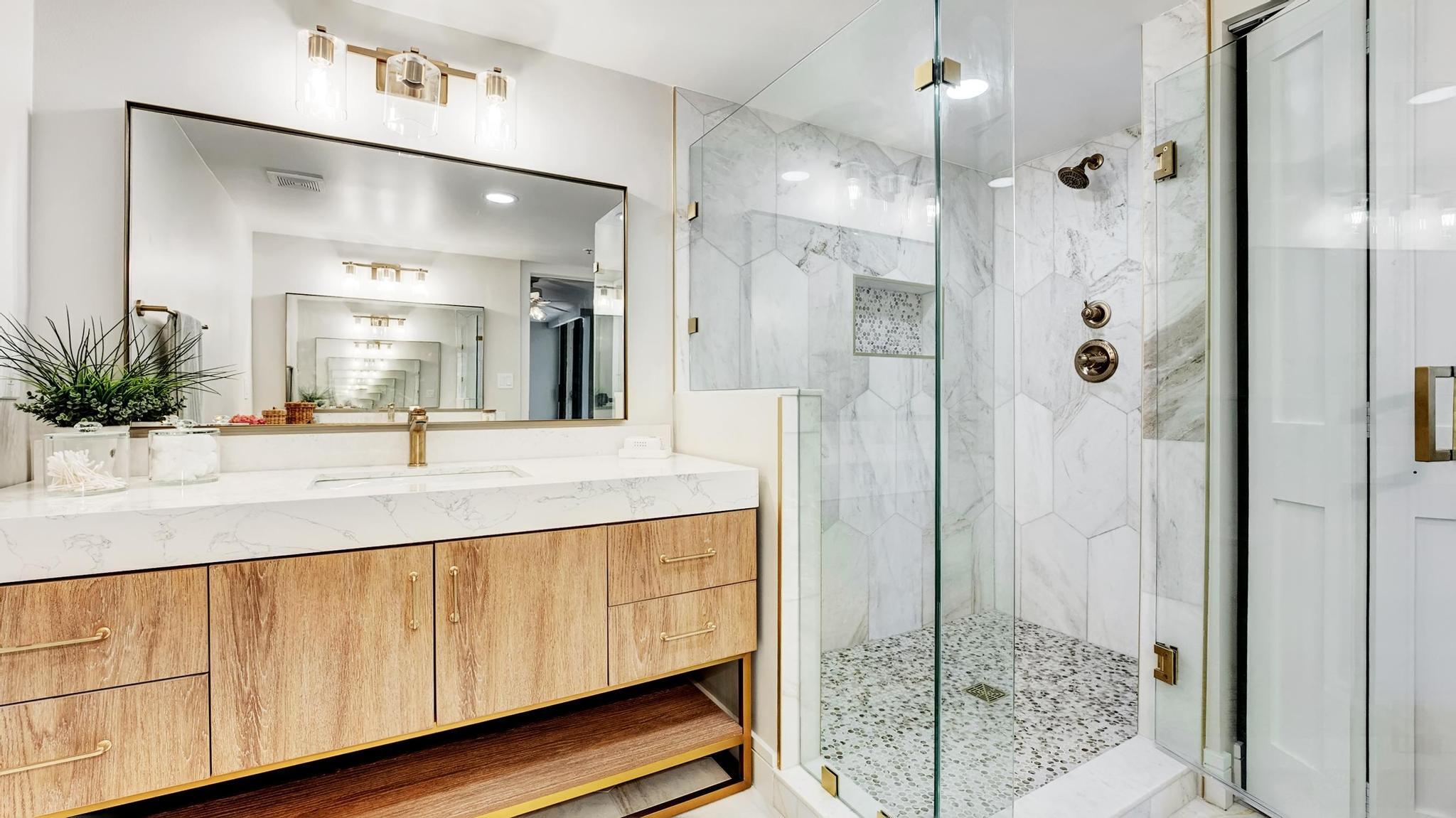 Bathroom with wood-front vanity and glass-enclosed marble shower with pebble floor.