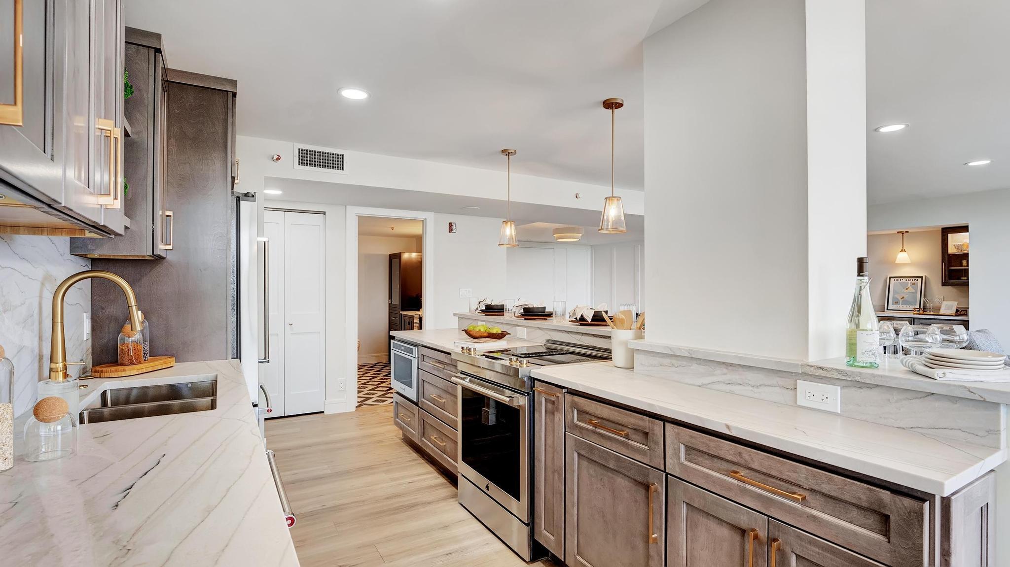 Contemporary kitchen with a large stone island, gray cabinetry, and gold fixtures.