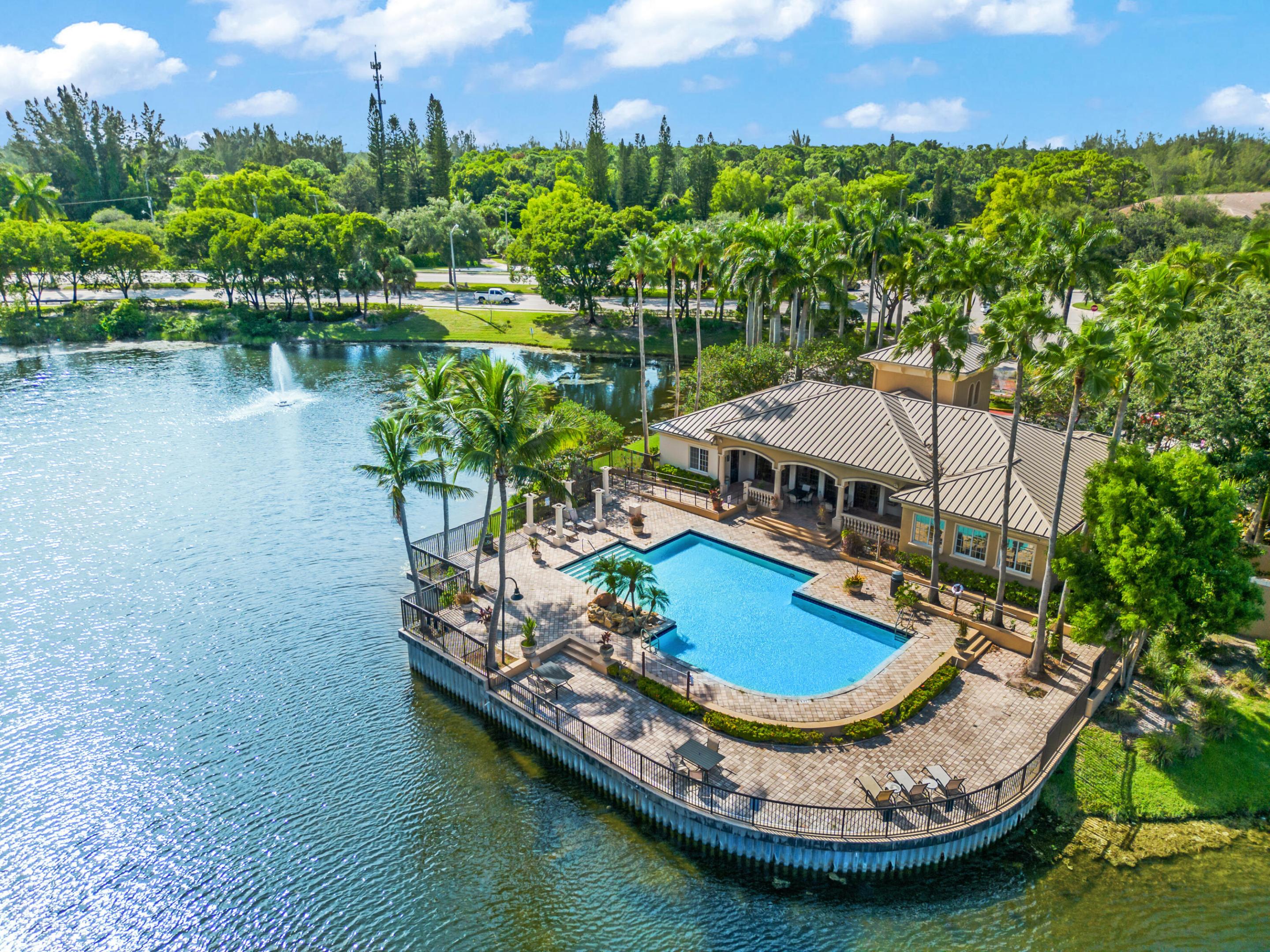 Waterfront clubhouse and pool beside a lake, surrounded by palm trees.