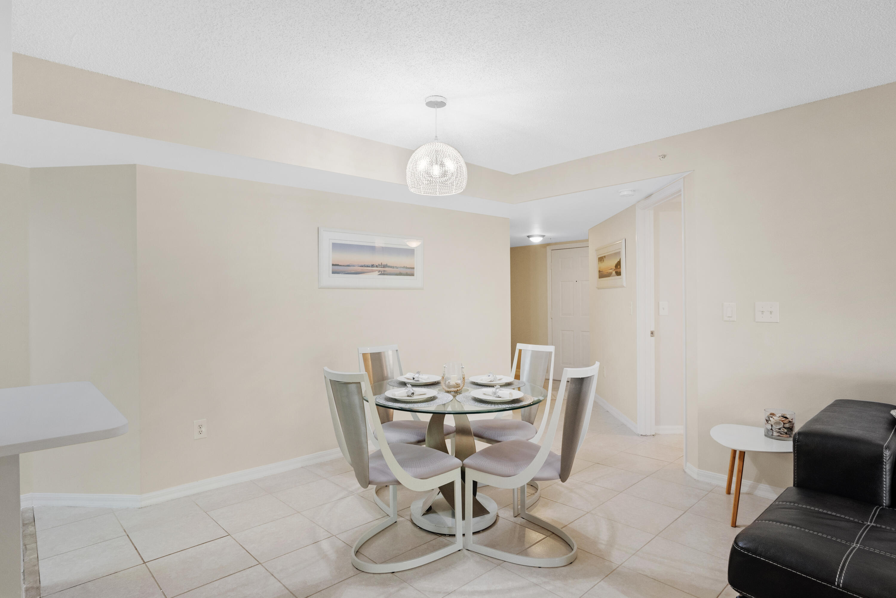 Dining area with a set glass table, curved white chairs, and a crystal pendant light.