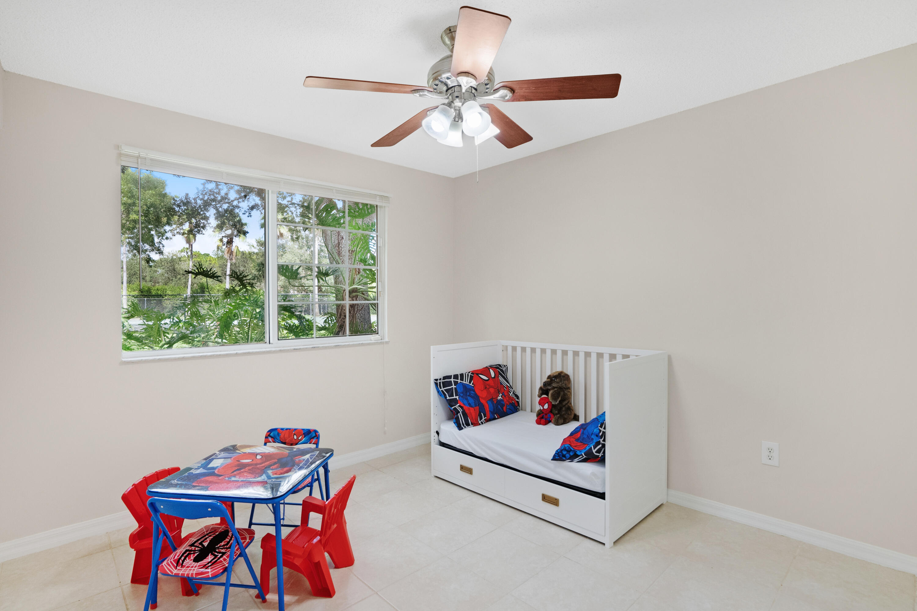 Child's bedroom with a white daybed, Spider-Man decor, and a window overlooking tropical greenery.