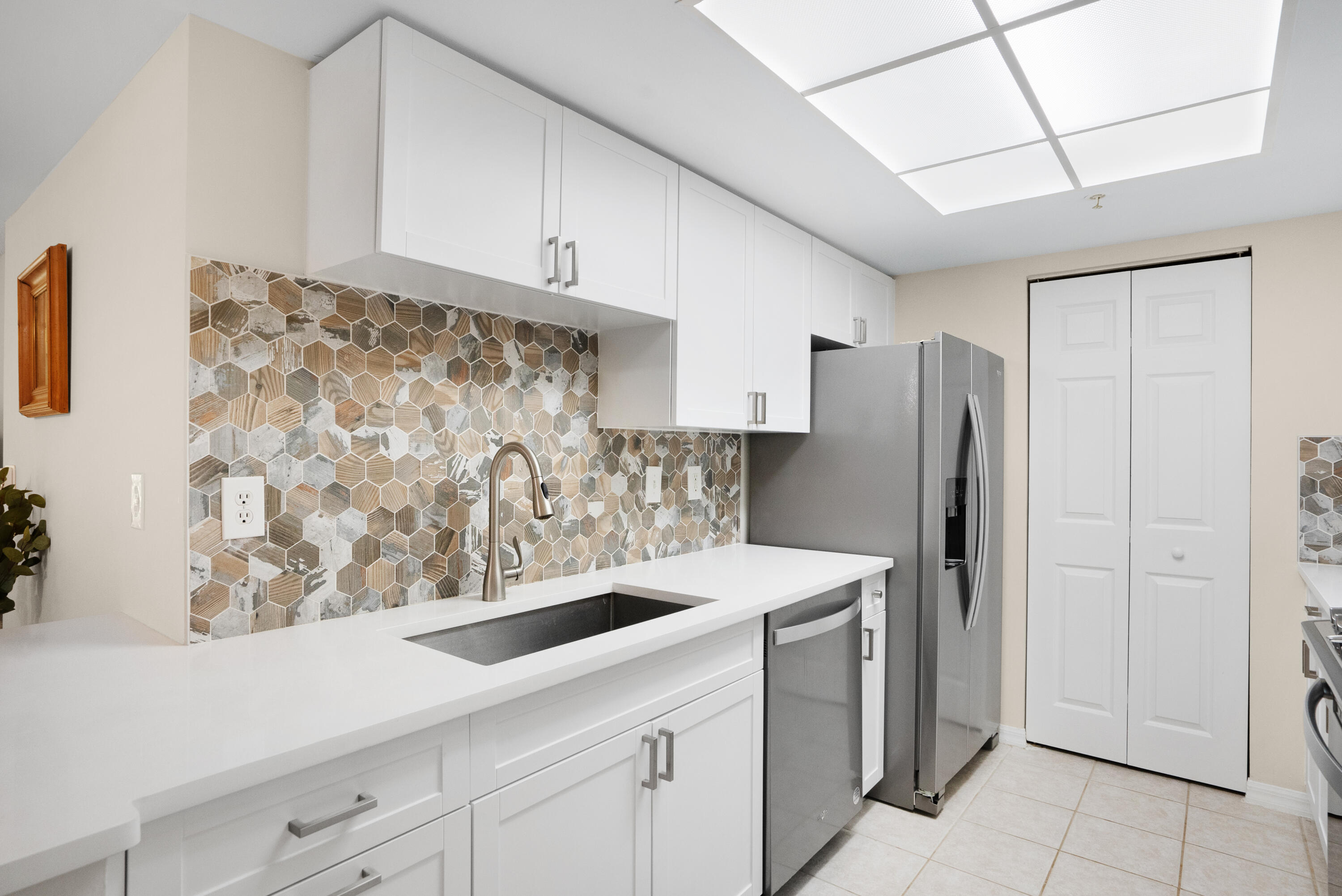 Kitchen with white cabinetry, patterned hexagonal backsplash, and stainless steel appliances.