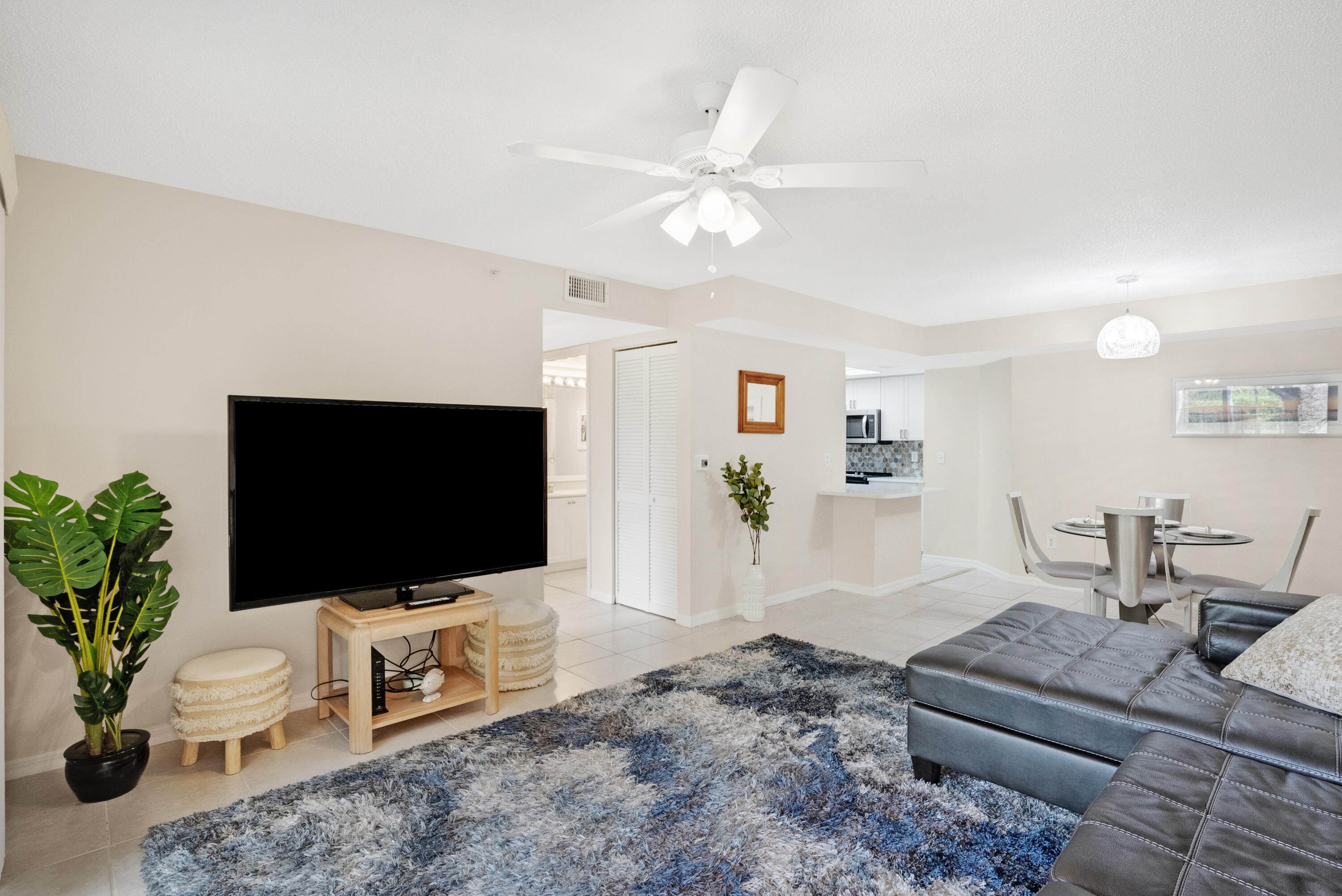 Open-plan living room with a gray sectional, large rug, and dining area beside the kitchen.