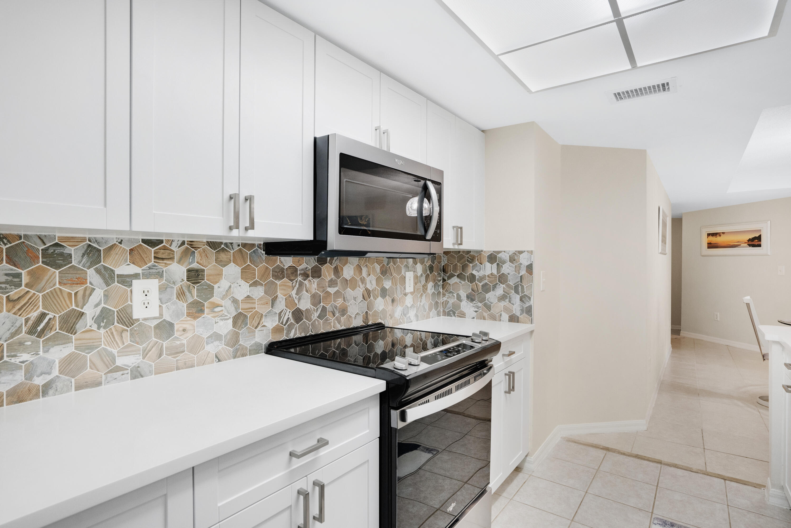 Kitchen with white cabinetry, geometric tile backsplash, and black range and microwave.