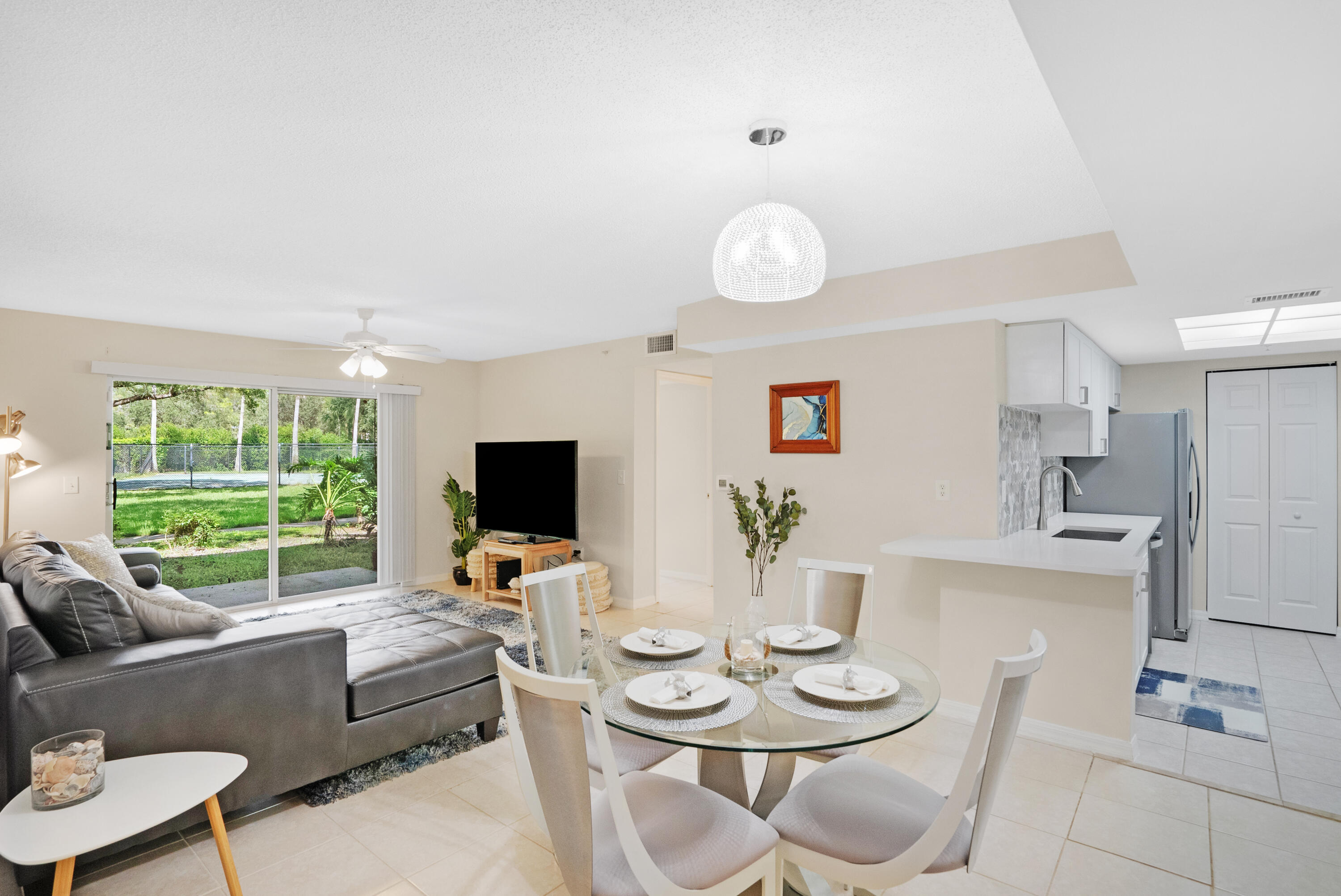 Open-plan living and dining area with a gray sectional, glass table, and sliding doors to a grassy yard.