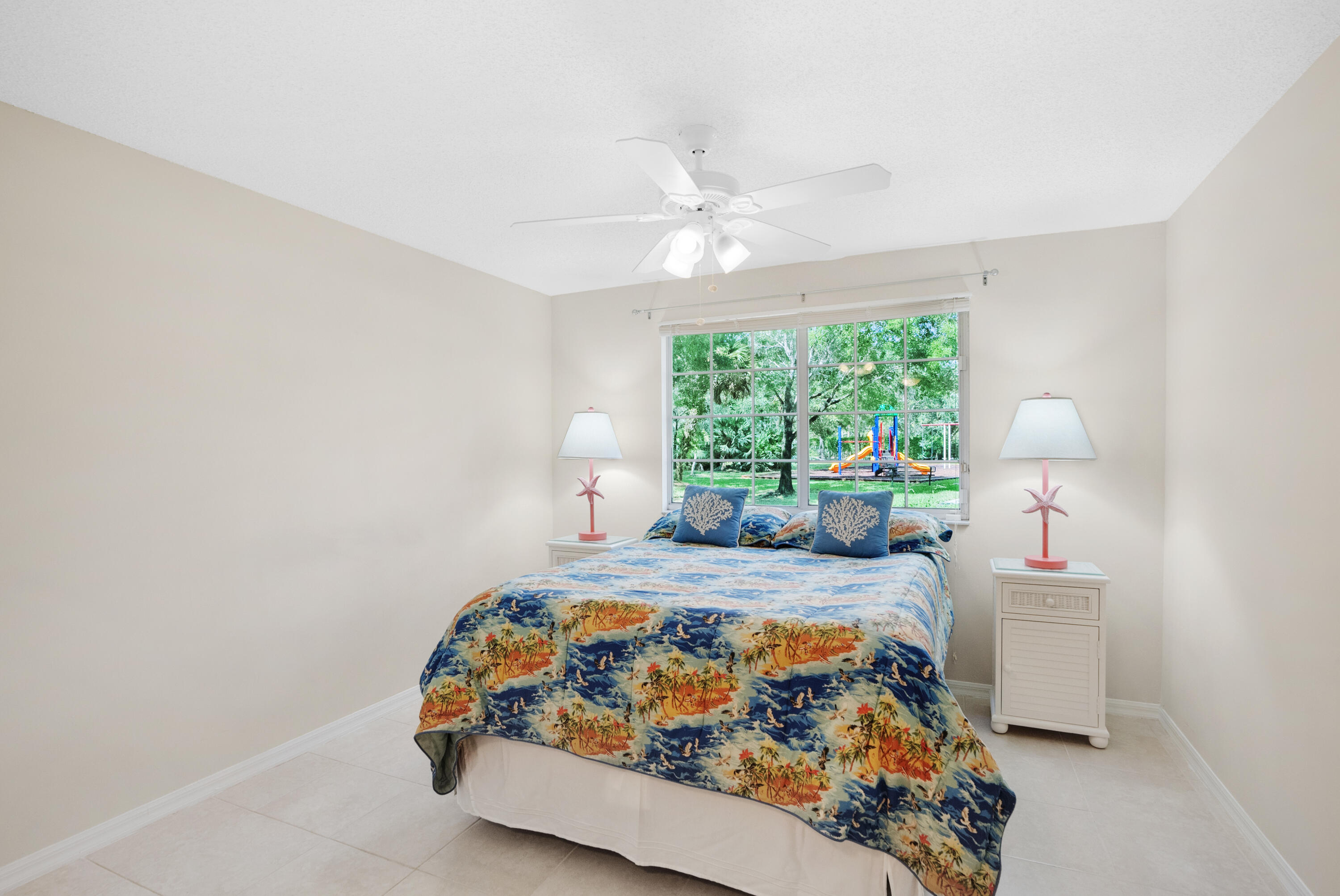 Bedroom with a tropical-patterned bedspread and a window overlooking a playground.
