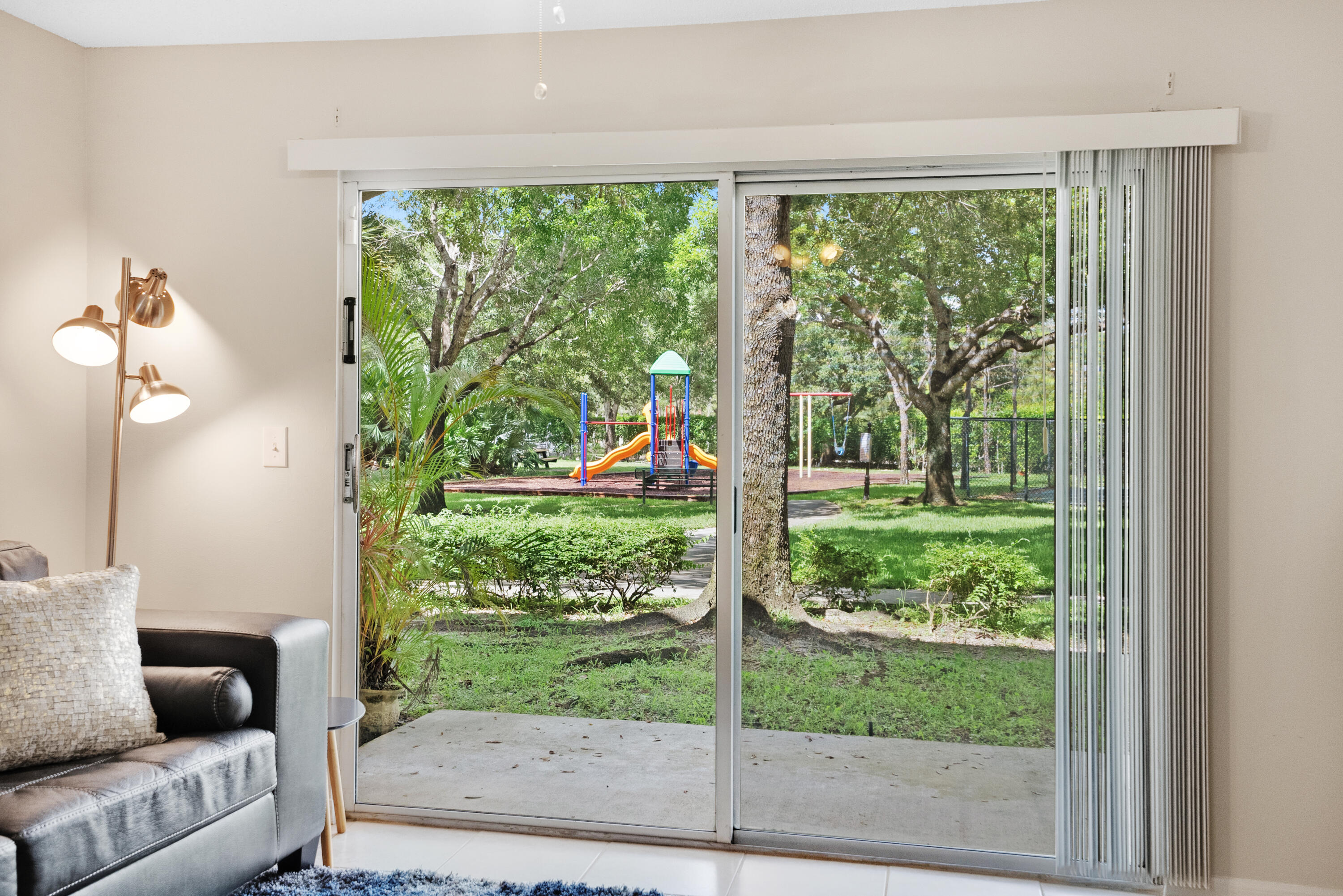 Living room with sliding glass doors overlooking a leafy playground and patio.