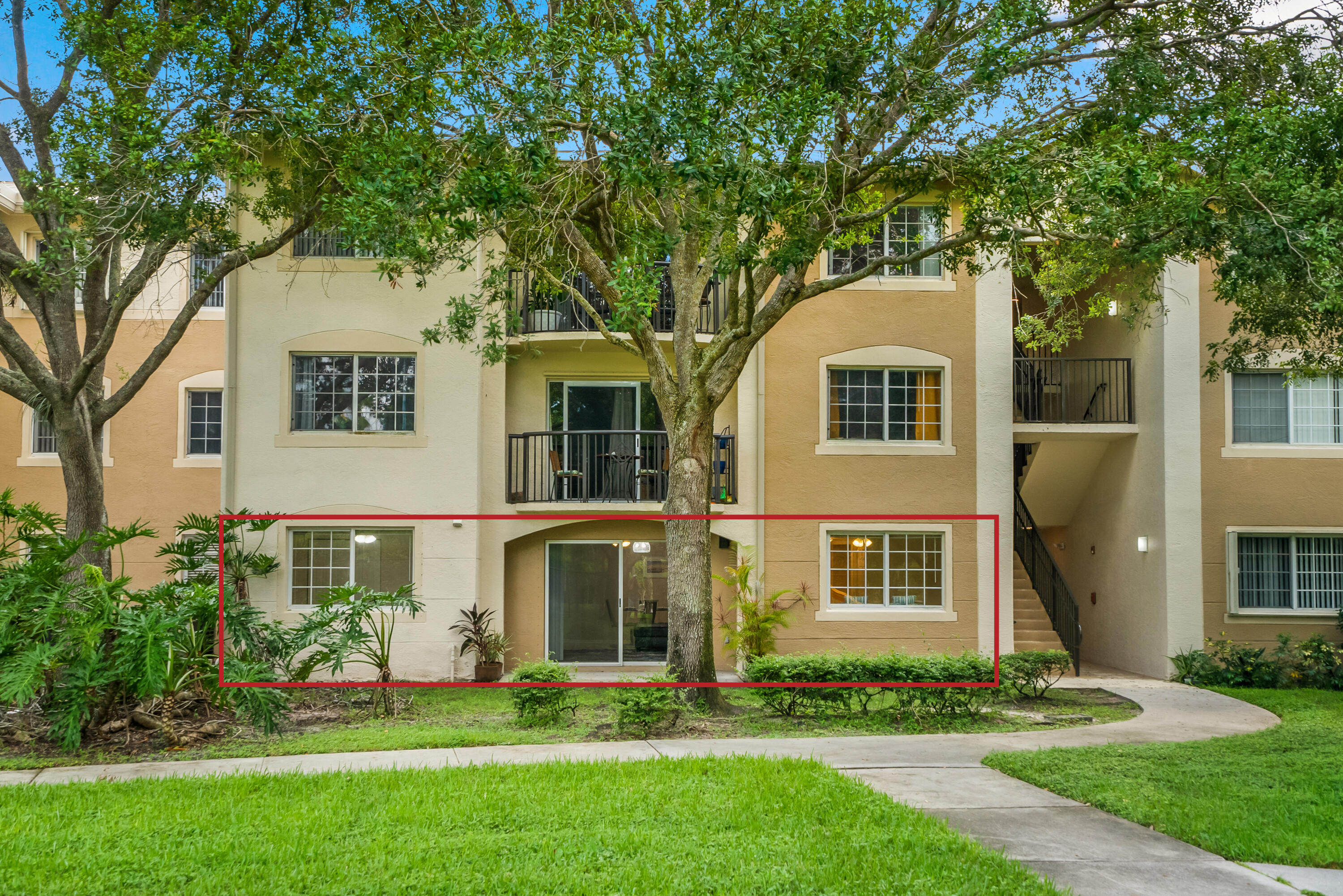 Condominium exterior with a red outline highlighting a ground-floor unit beneath mature trees.