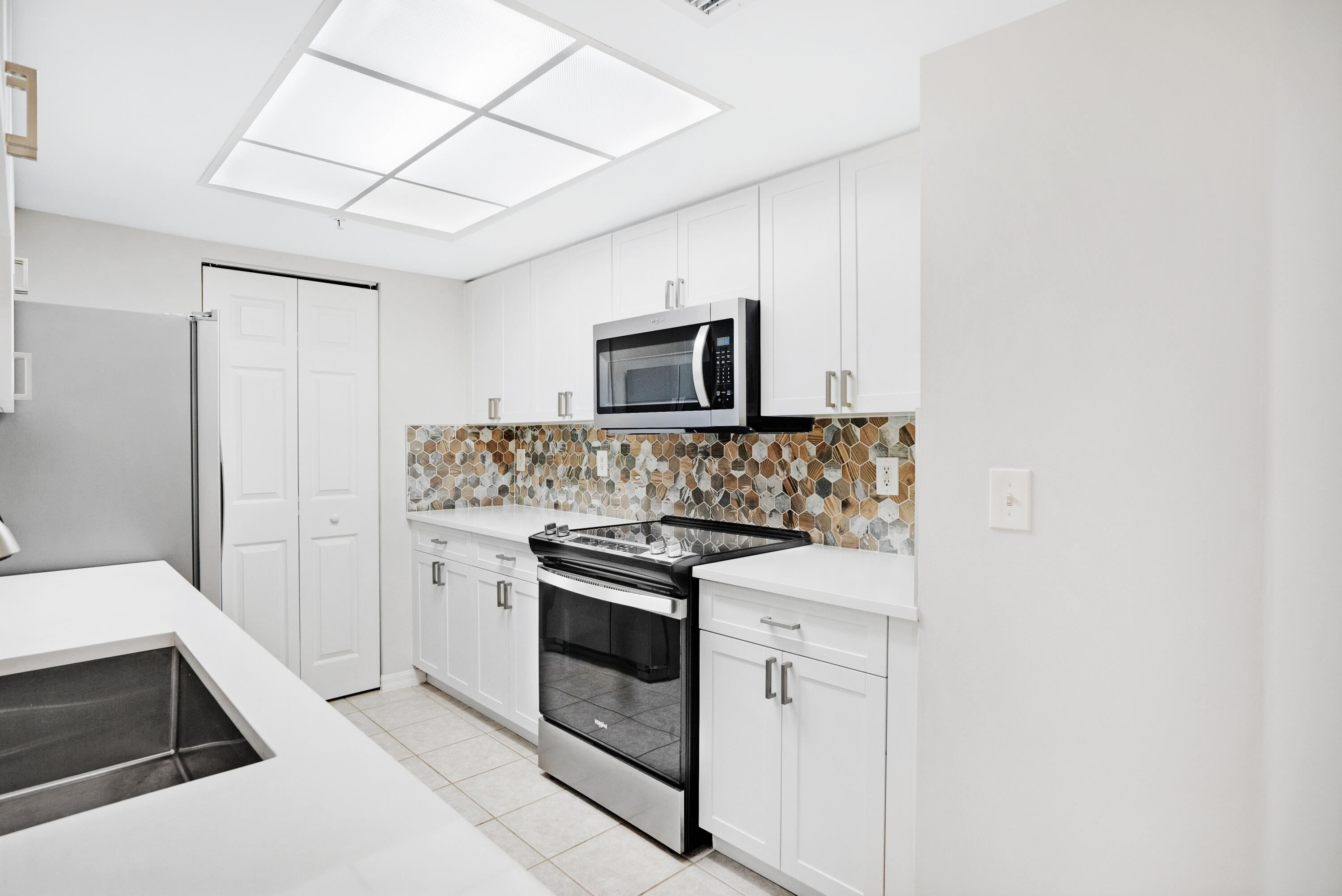 Kitchen with white cabinets, black appliances, and a multicolored hexagonal tile backsplash.