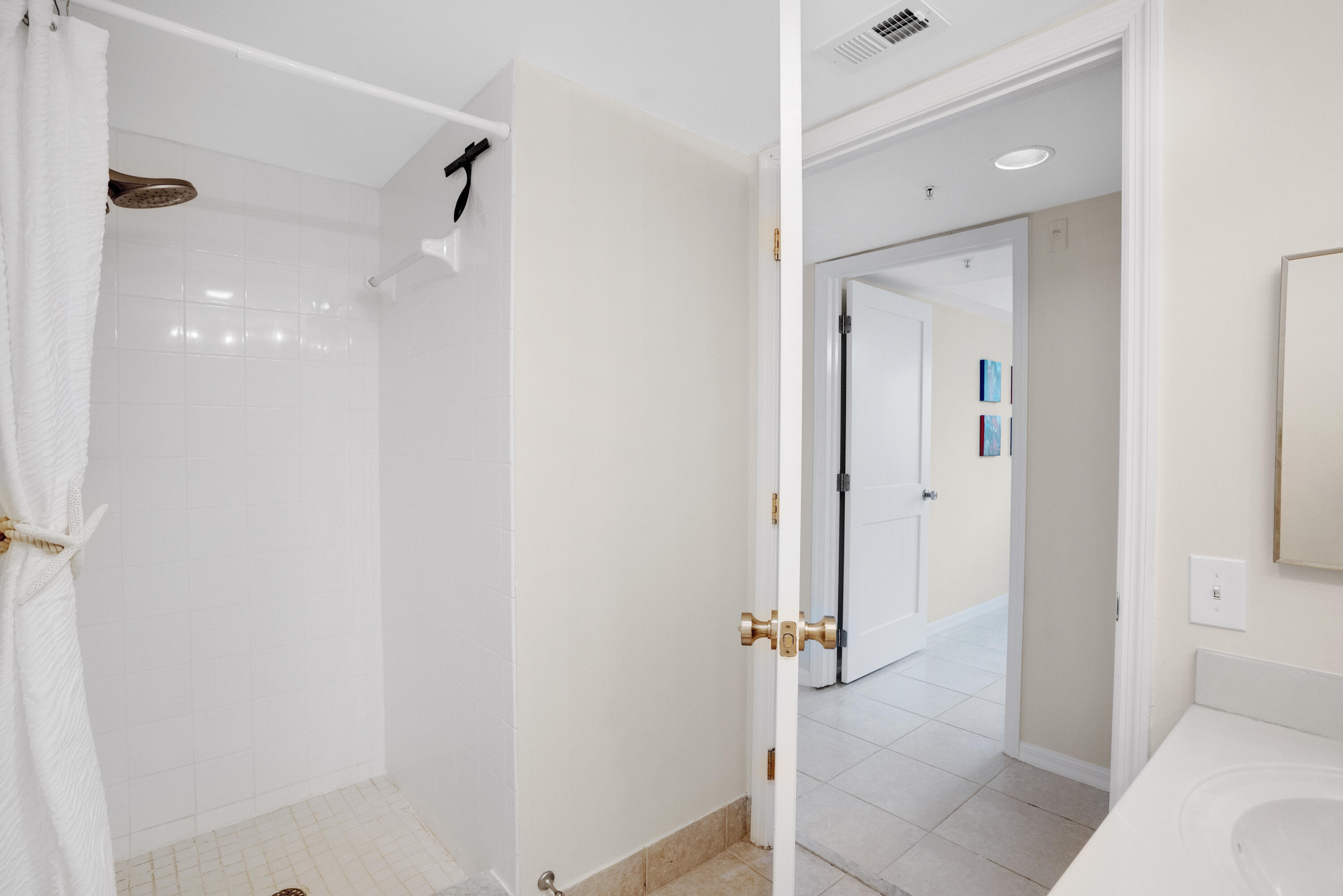 Bathroom with a tiled walk-in shower, tied-back curtain, and open door to the hallway.