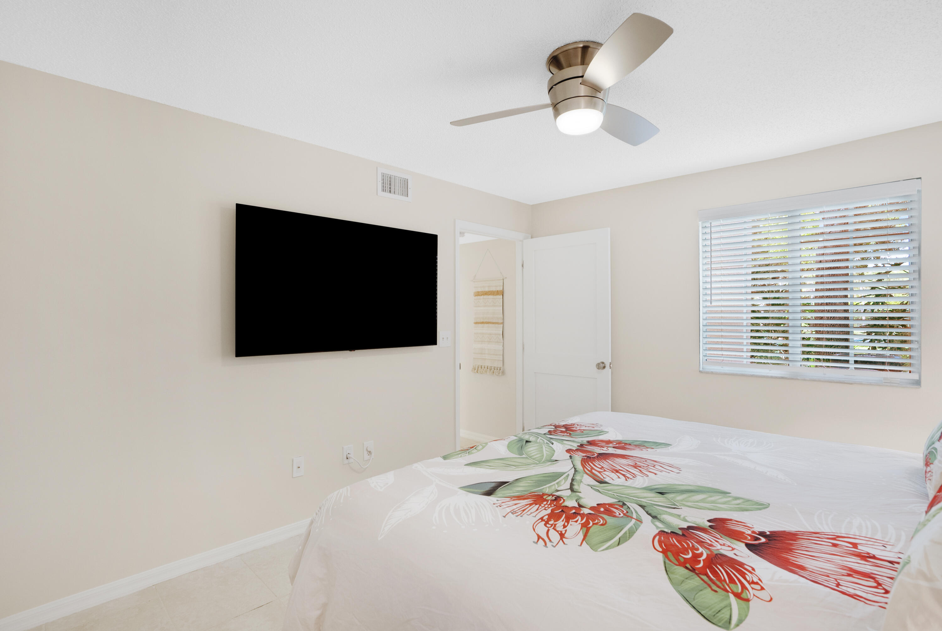 Bedroom with floral bedding, a wall-mounted television, and a ceiling fan.
