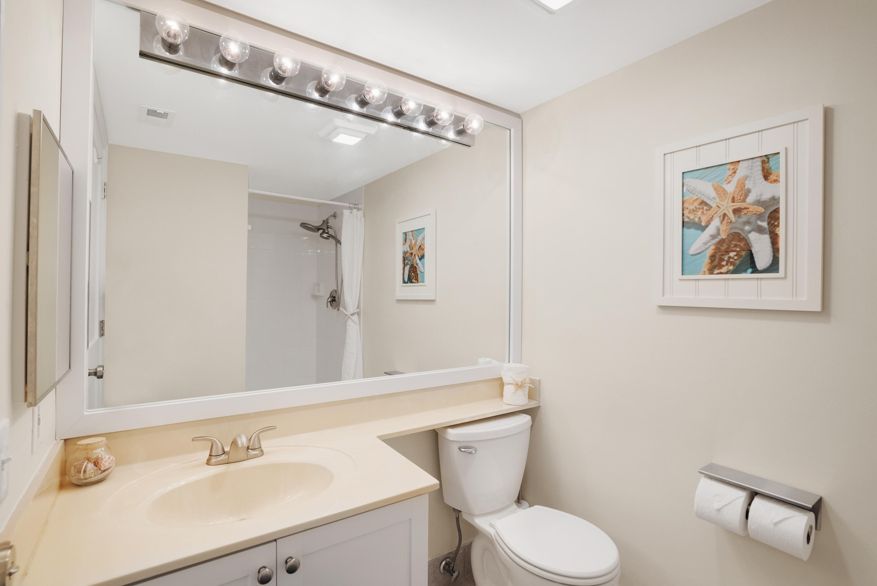 Bathroom with a cream vanity, large mirror, white toilet, and framed starfish artwork.