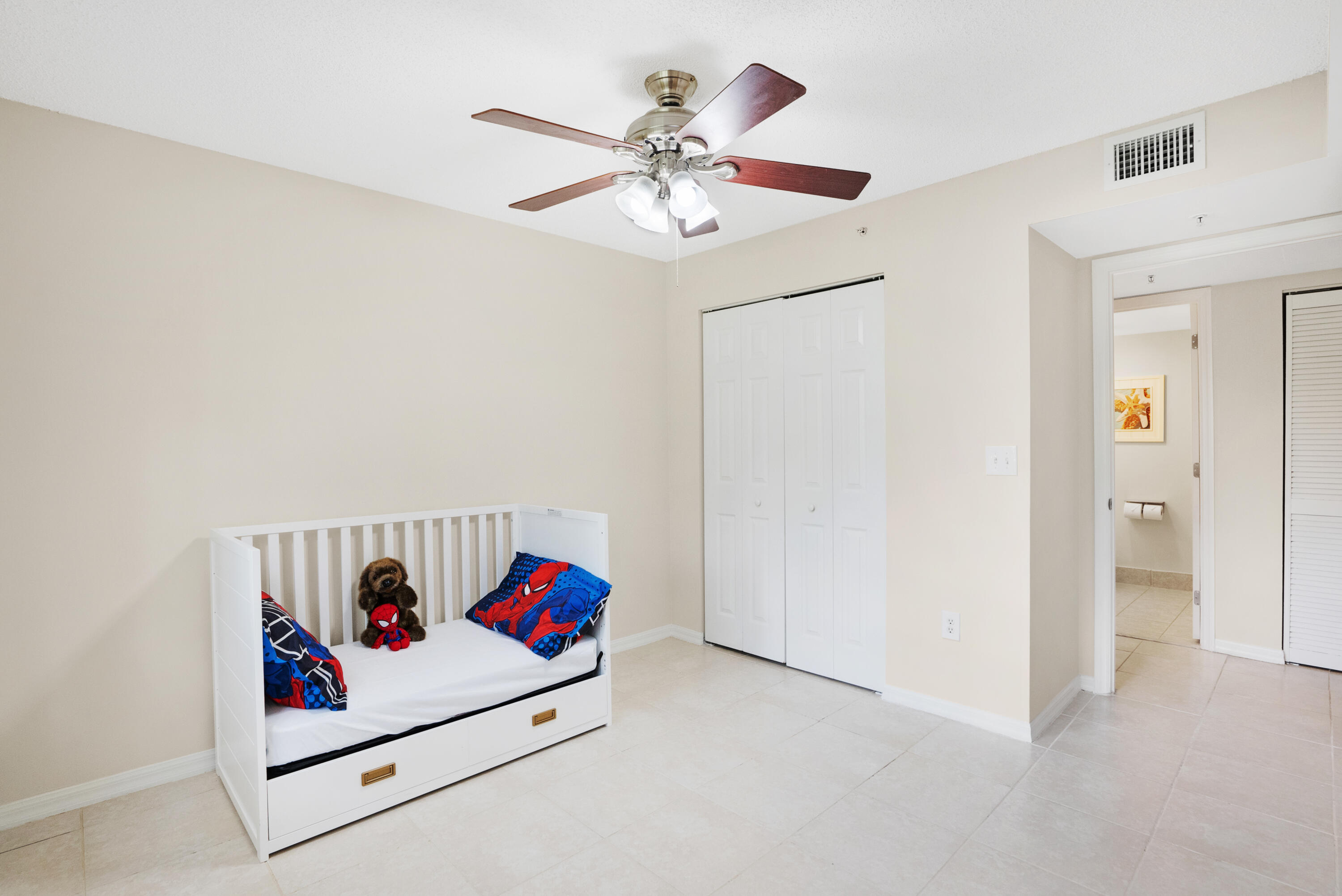 Bedroom with a white daybed, colorful superhero bedding, and a ceiling fan.