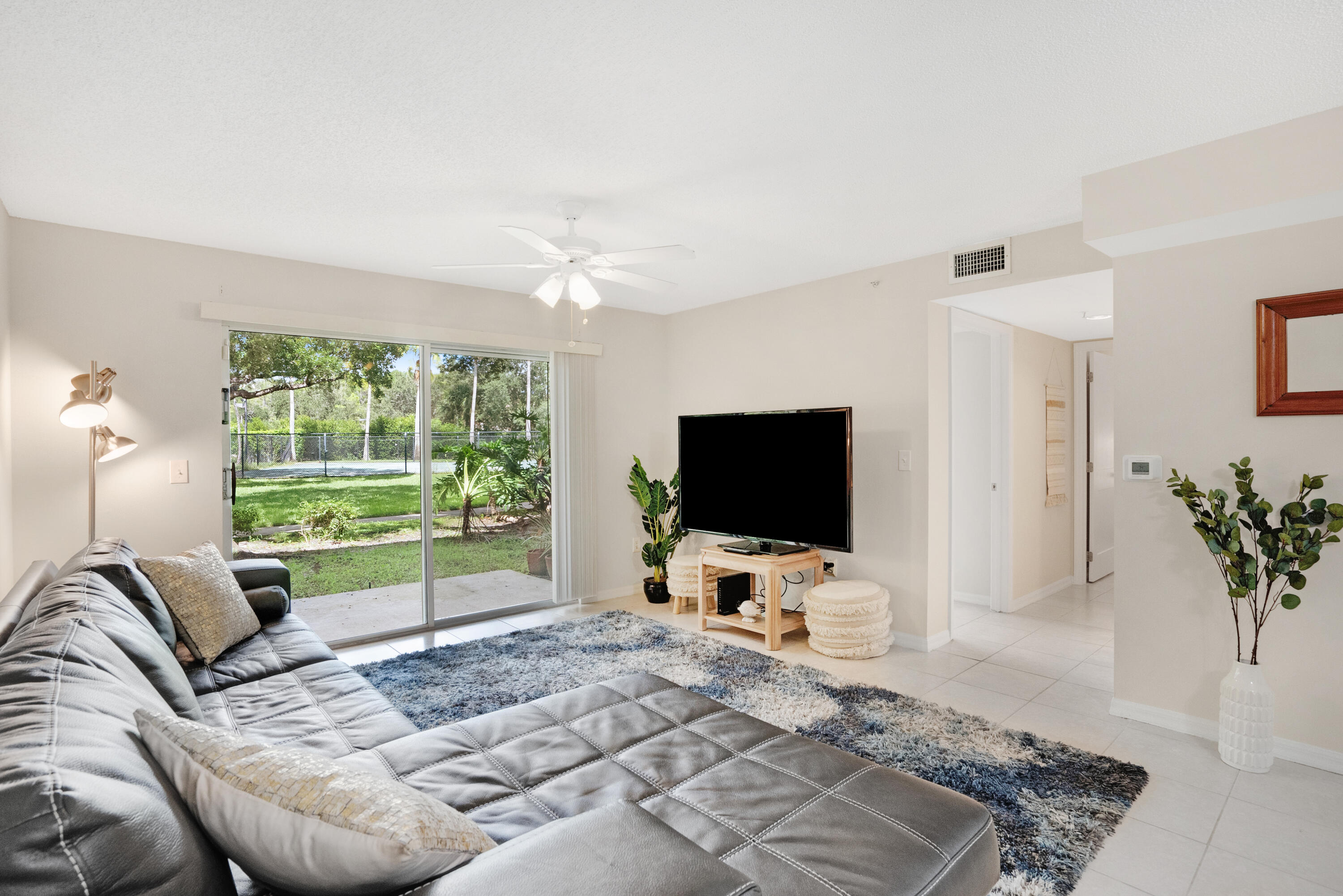 Living room with a gray sectional, television, and sliding doors overlooking a green yard.