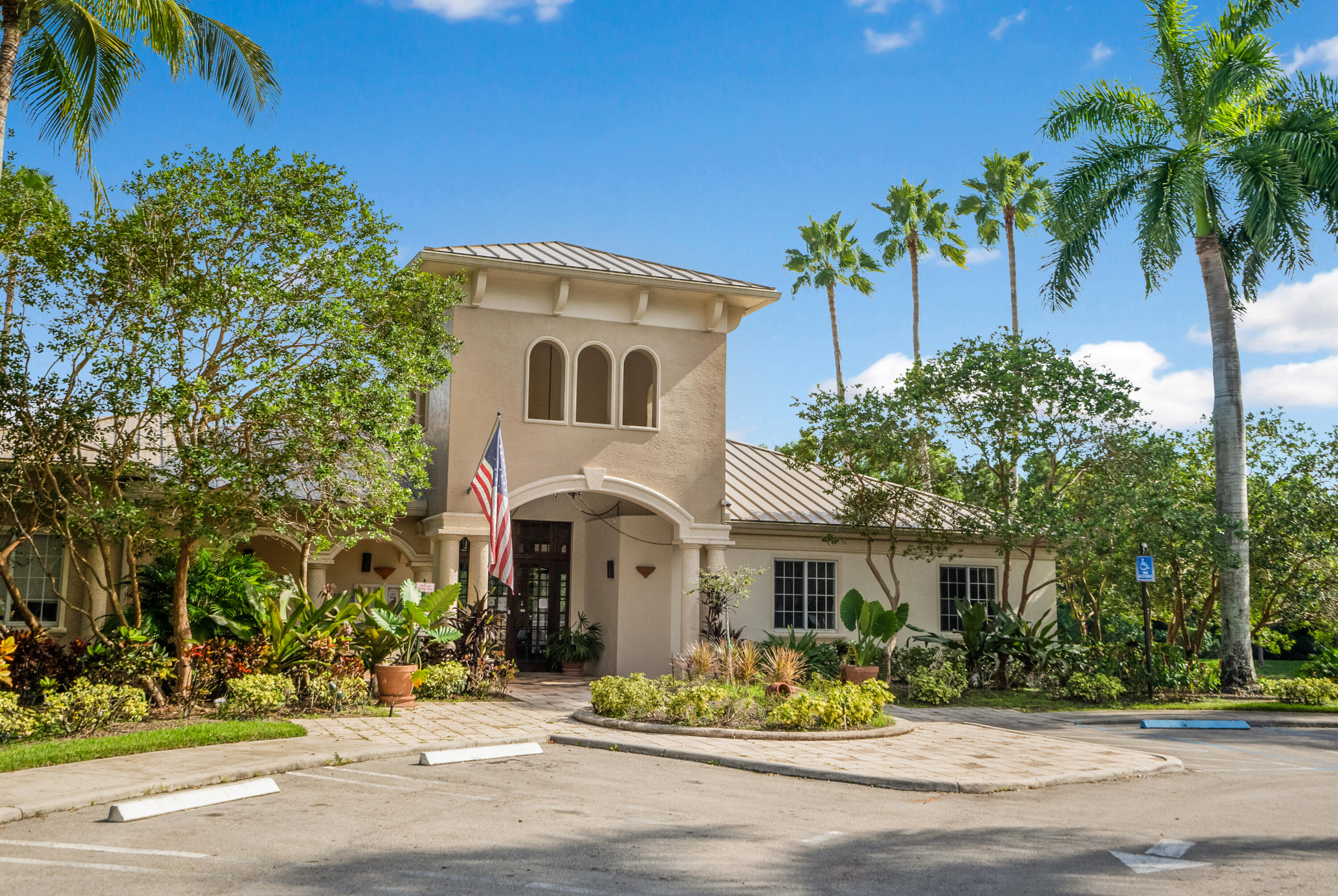 Tan residential building entrance with an American flag, tropical landscaping, and palm trees.