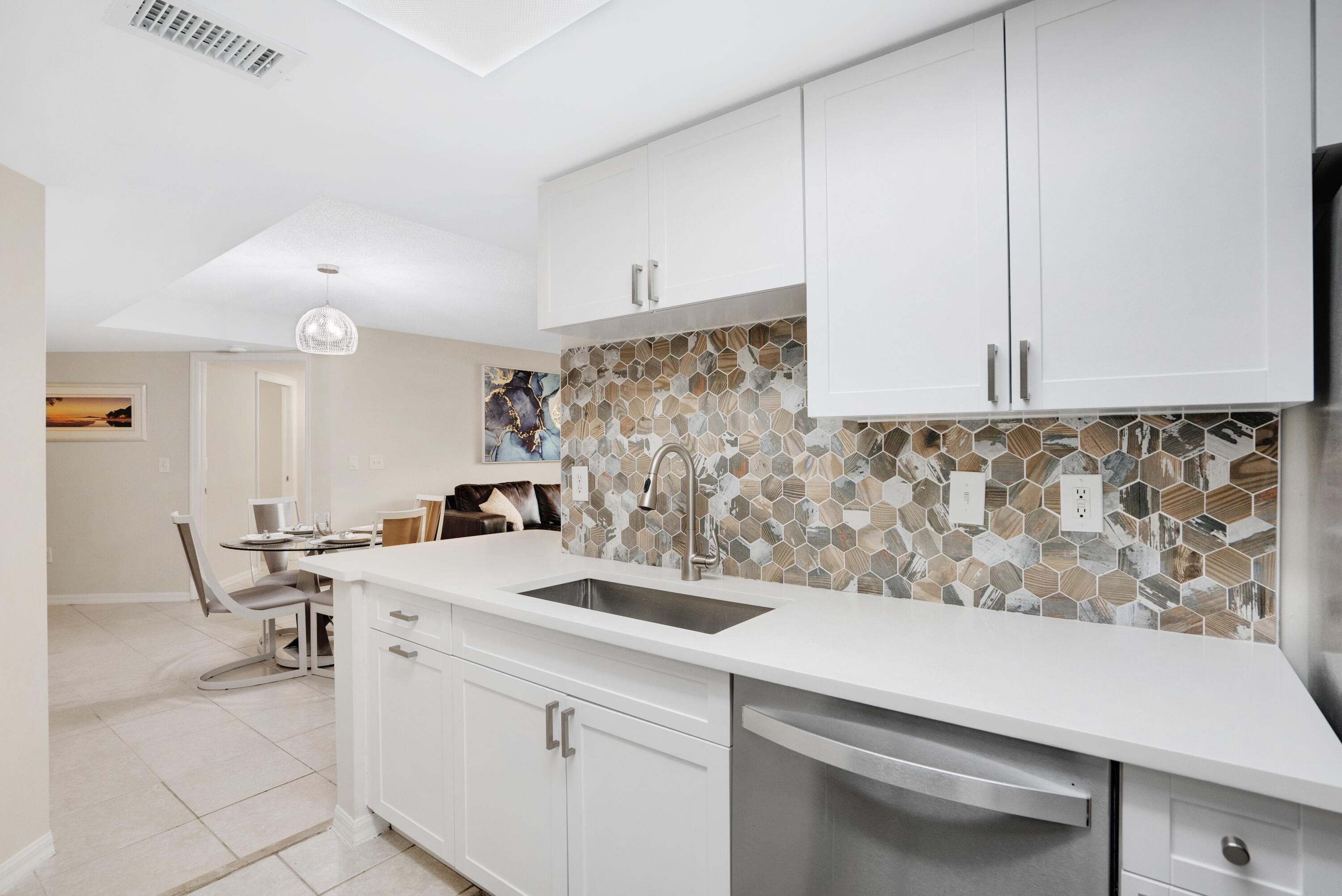 Renovated kitchen with white cabinetry, stainless steel dishwasher, and geometric tile backsplash.