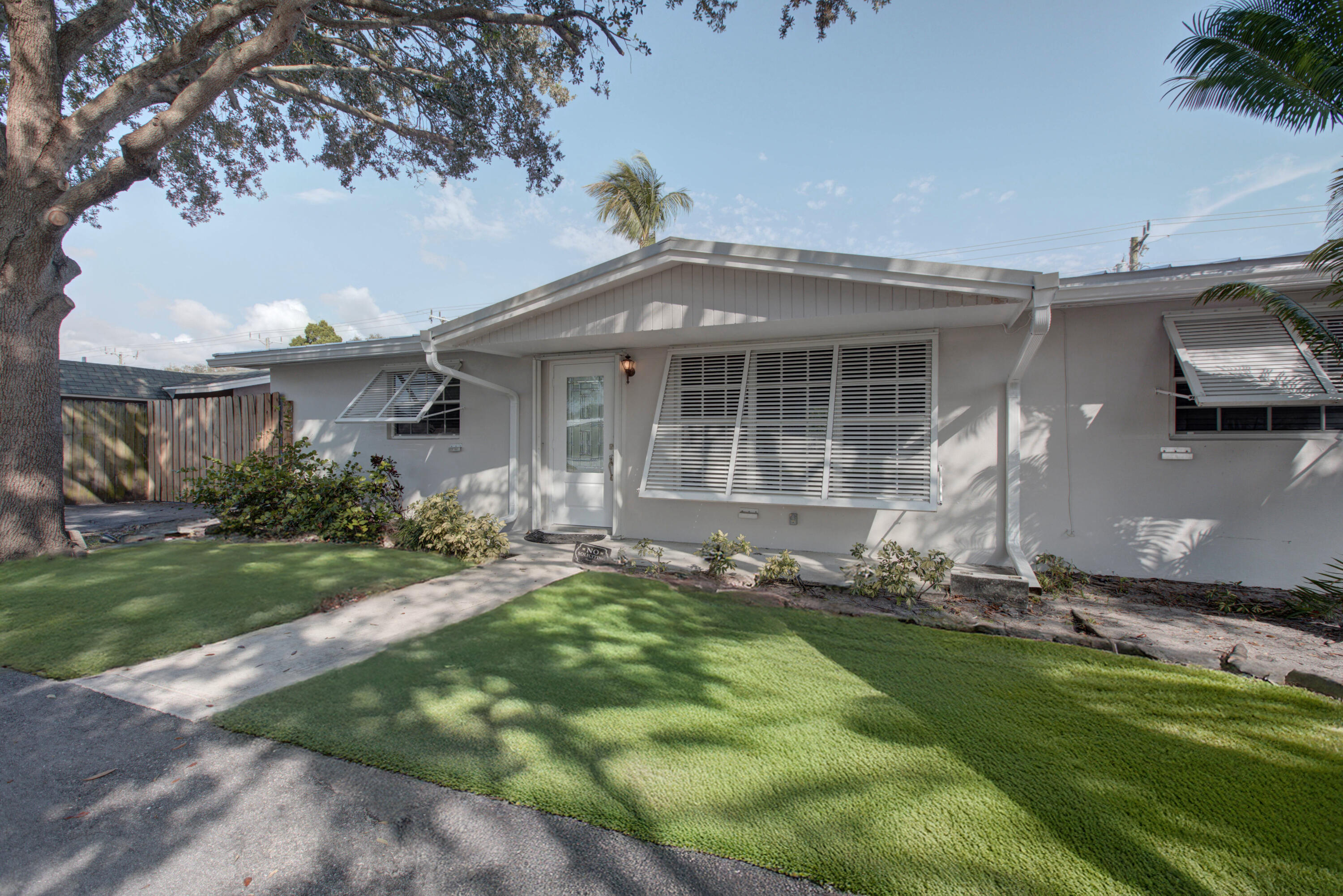Single-story home with white louvered shutters, a front lawn, and tropical landscaping.