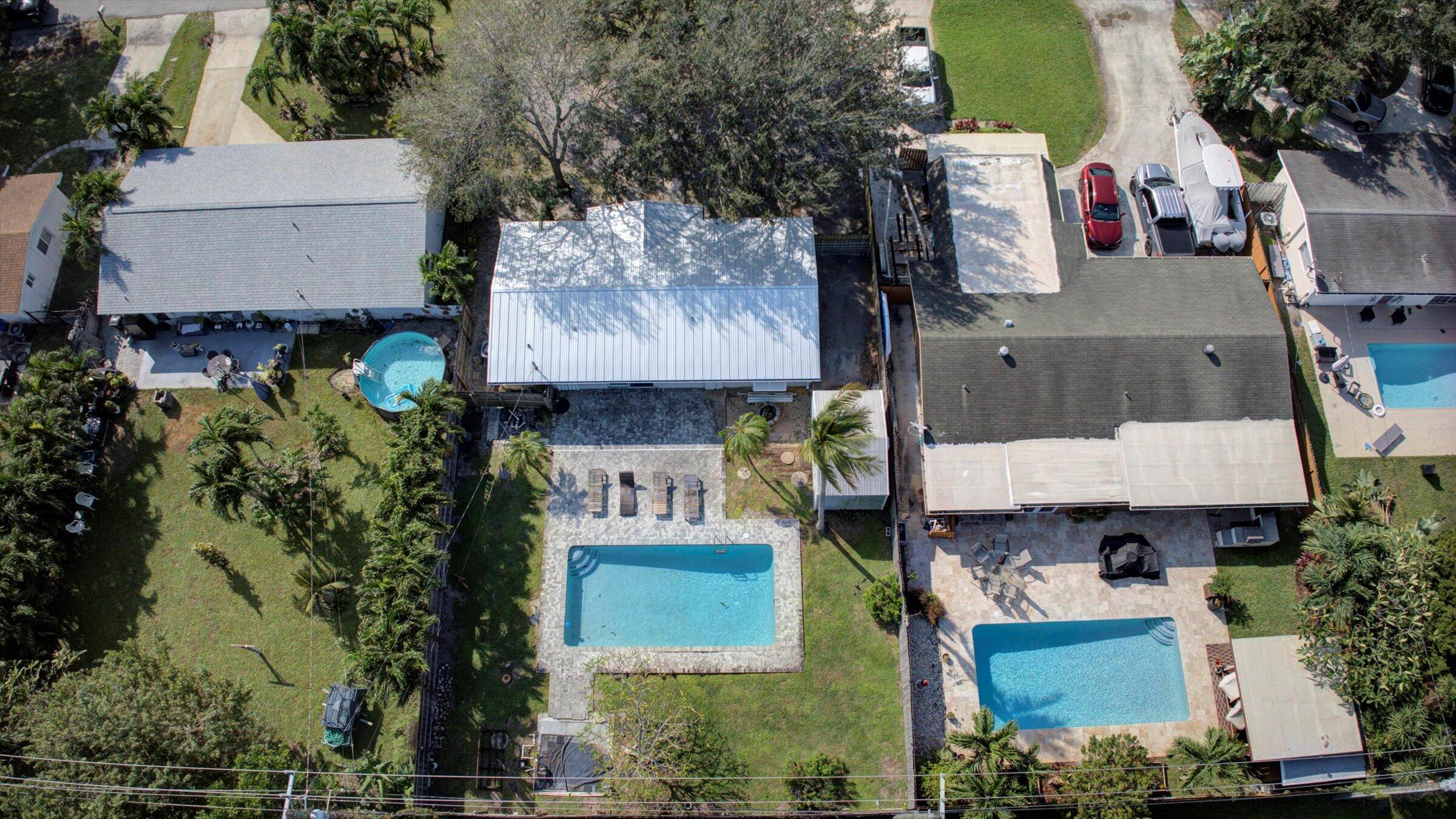 Aerial view of a home with a rectangular pool, paved deck, lawn, and palm trees.