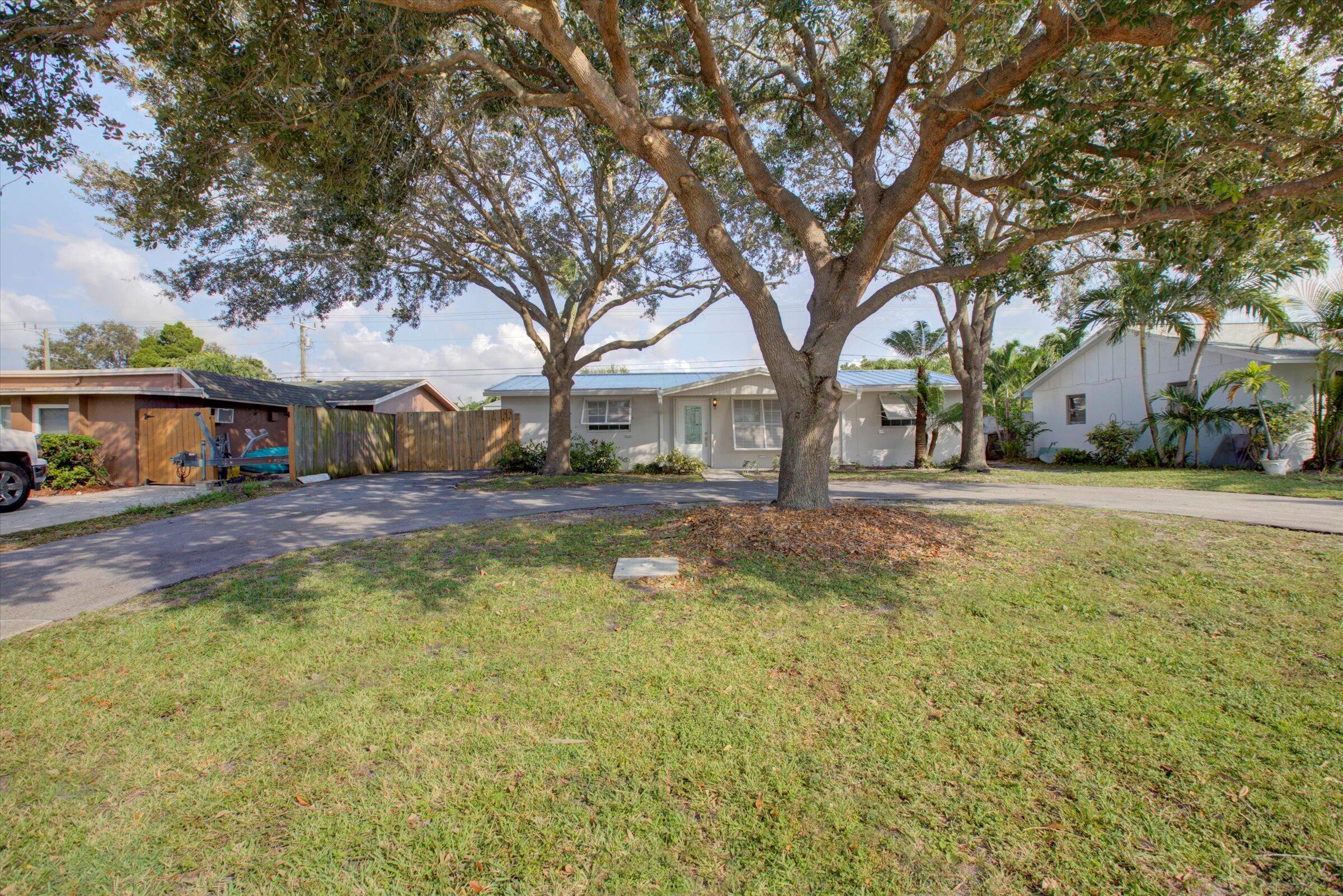 Single-story home behind large shade trees, with a broad lawn and paved driveway.