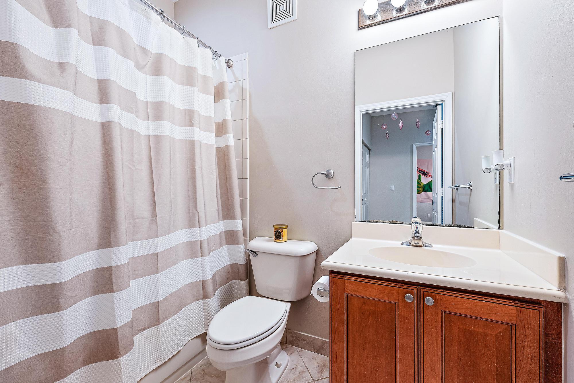 Bathroom with a striped shower curtain, white toilet, and wood vanity.