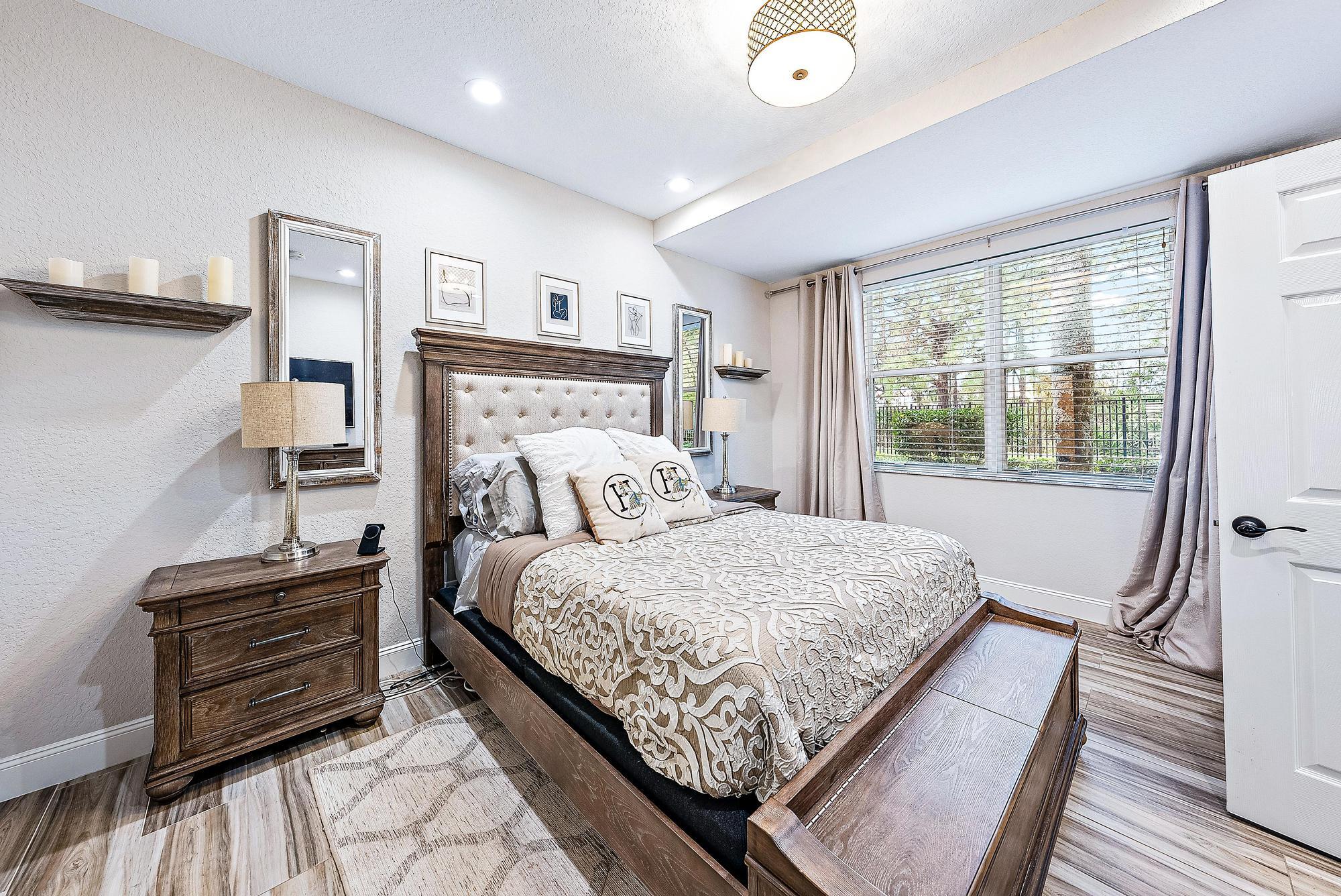 Bedroom with a dark wood bed, cream patterned bedding, and a wide curtained window.