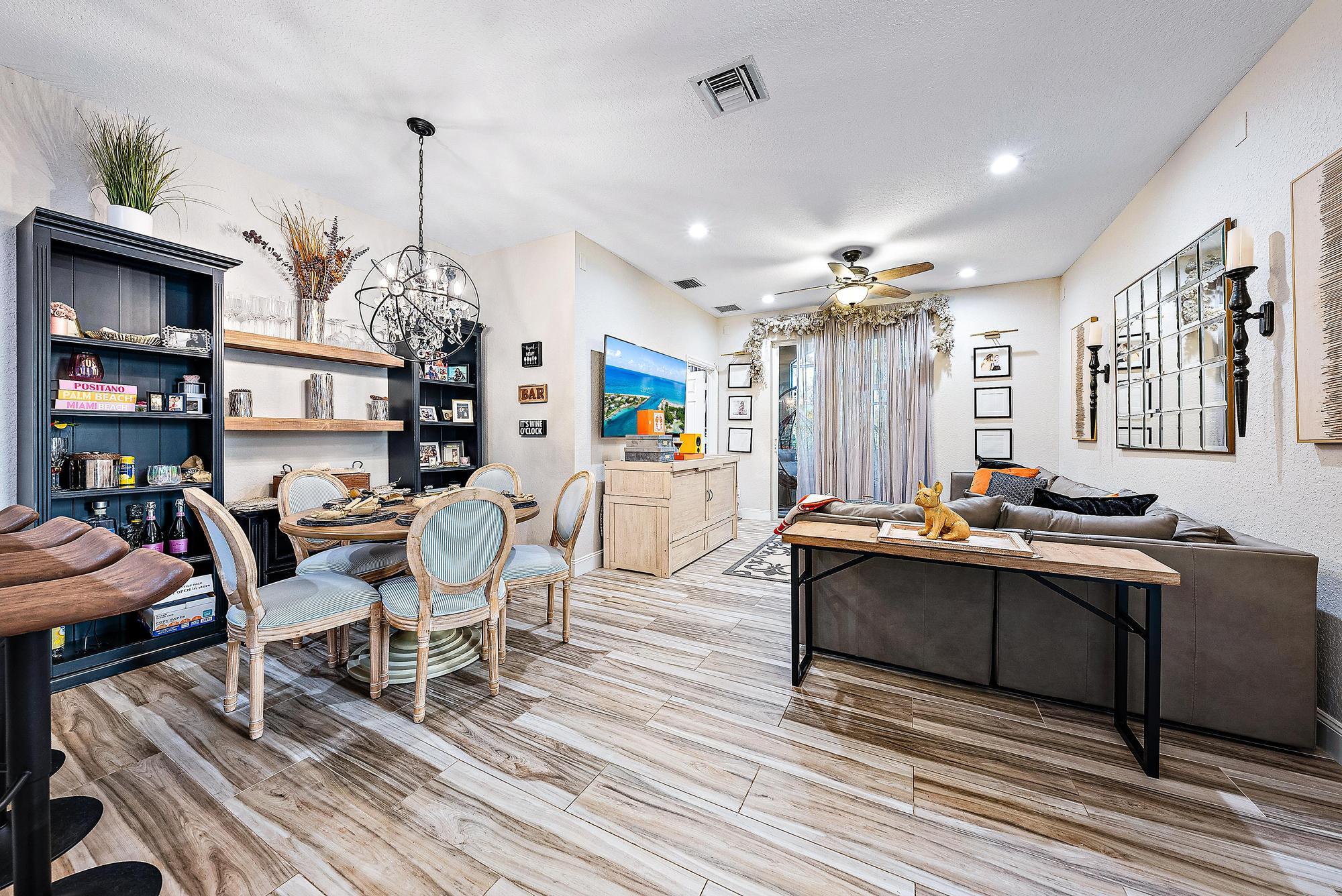 Open-plan living and dining room with dark built-in shelves, a gray sectional, and wood-look tile floors.