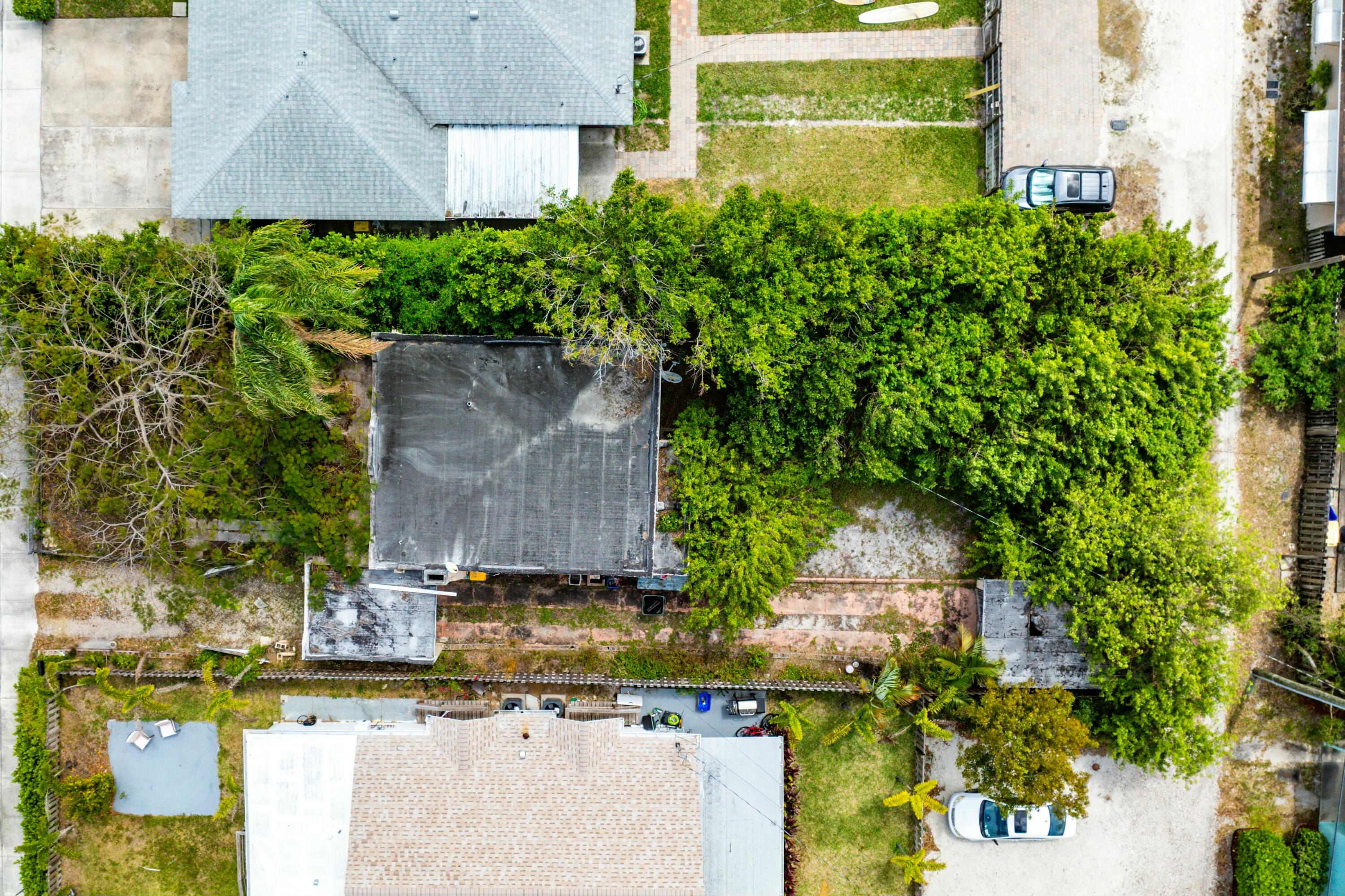 Aerial view of a tree-covered residential property with a dark-roofed structure and paved paths.