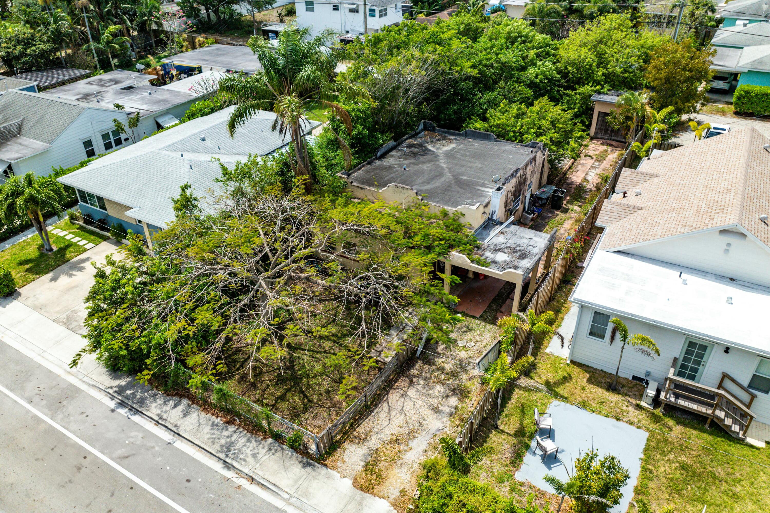 Aerial view of a flat-roof home on a tree-filled, fenced lot among neighboring houses.