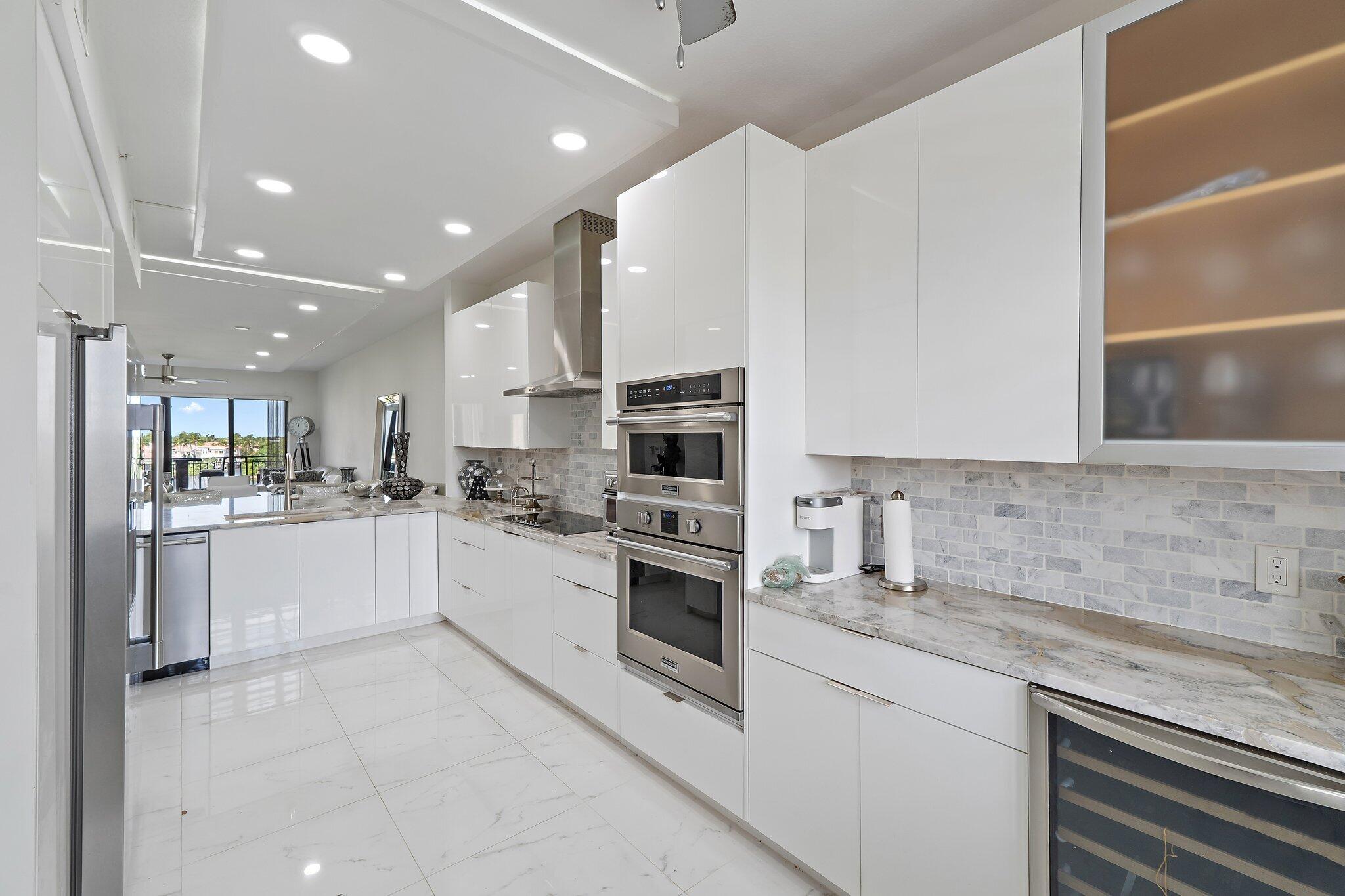 Modern white kitchen with marble counters, stainless steel double oven, and sliding doors to a balcony.