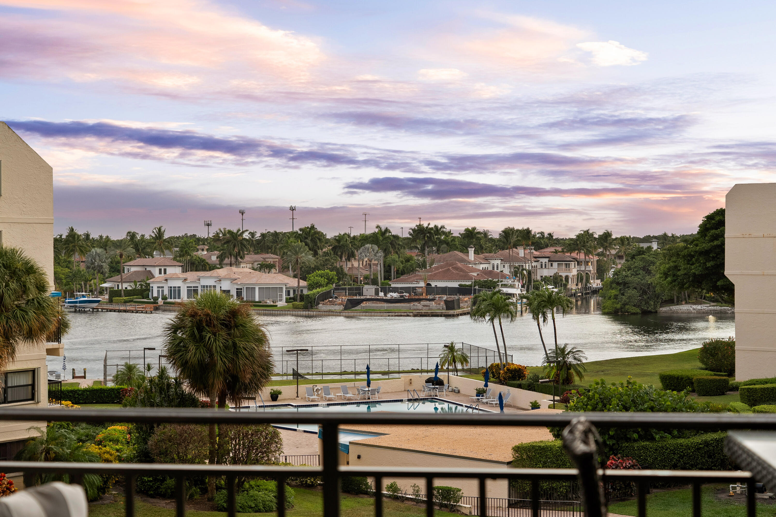 Balcony view over a waterway, with palm-lined homes and a swimming pool at dusk.
