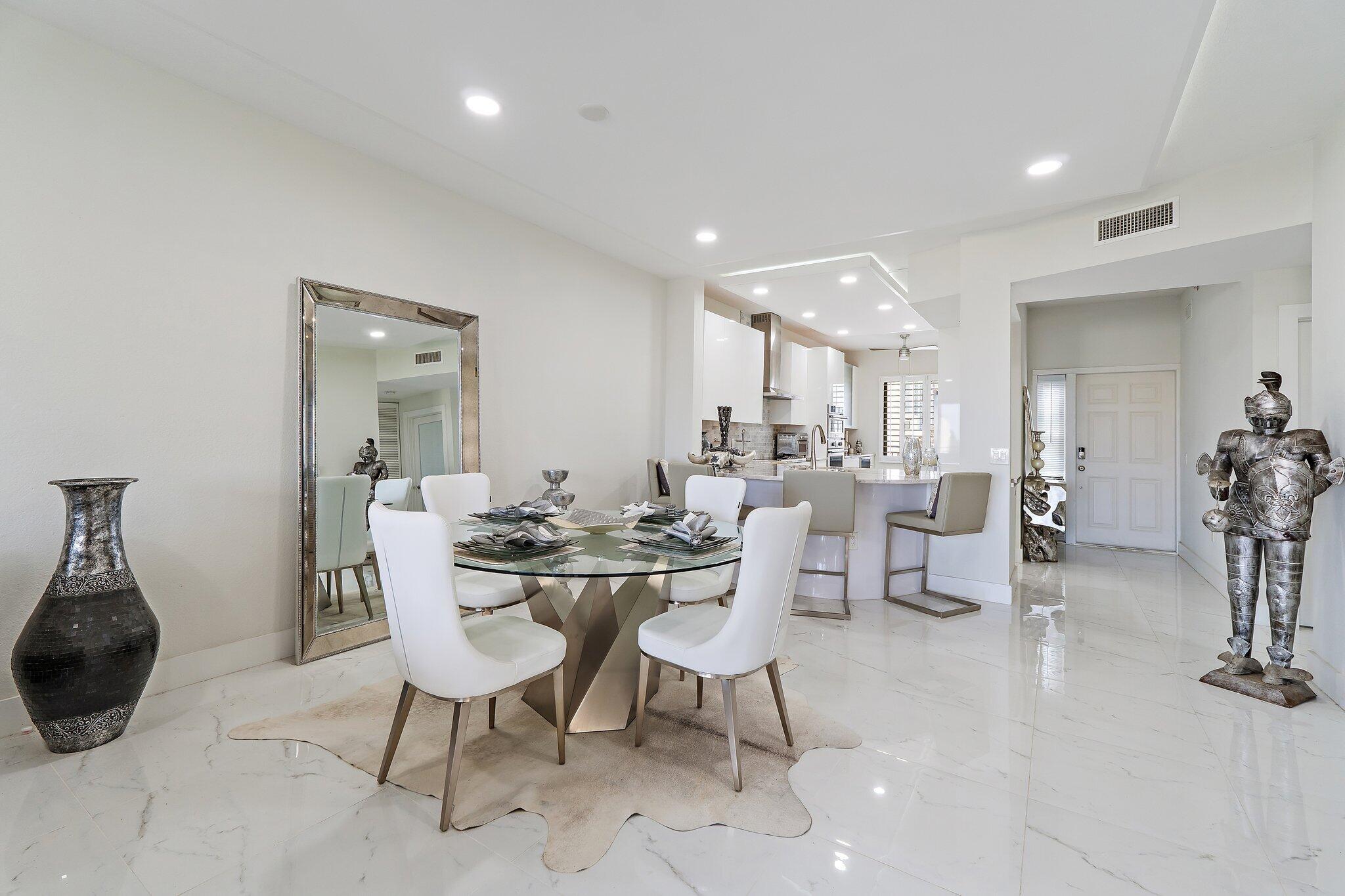 Dining area with a glass table and white chairs, opening into a modern kitchen.