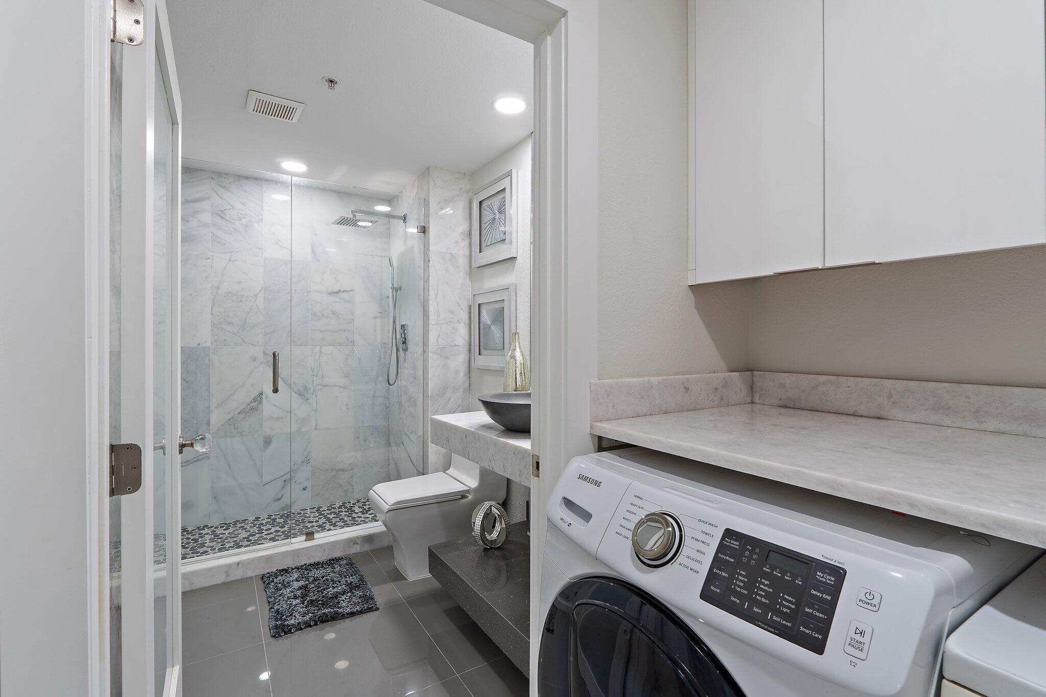 Modern bathroom with a marble walk-in shower and a Samsung washer and dryer under the counter.