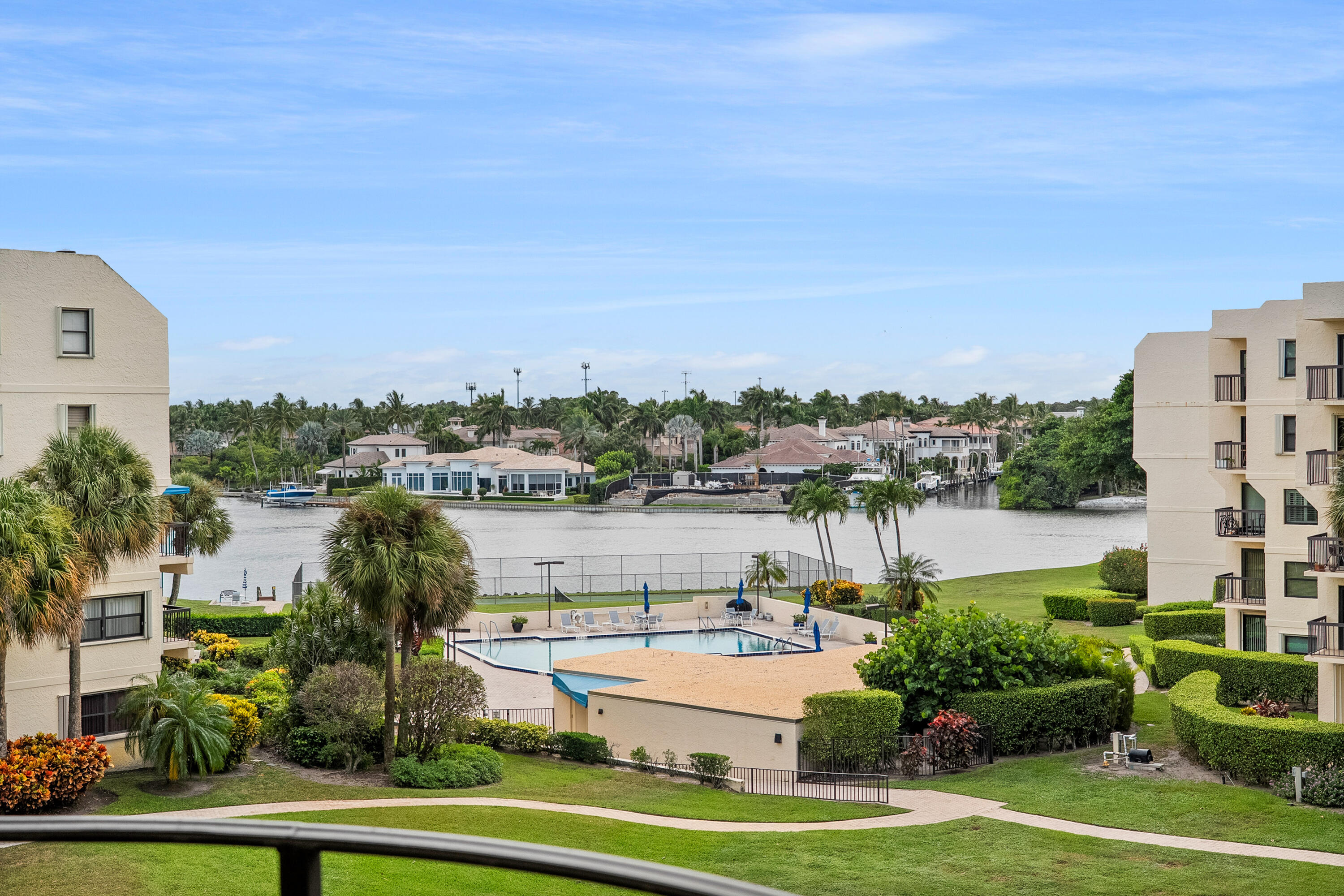 Condominium pool and landscaped grounds overlooking a palm-lined waterway and waterfront homes.