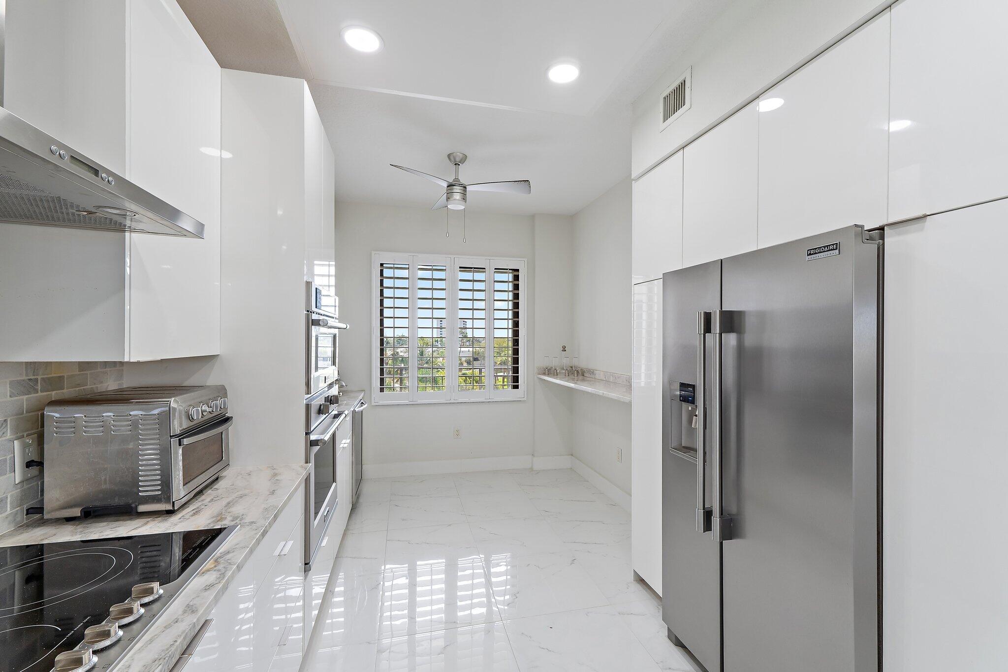 Bright kitchen with white cabinets, stainless steel appliances, and plantation shutters.