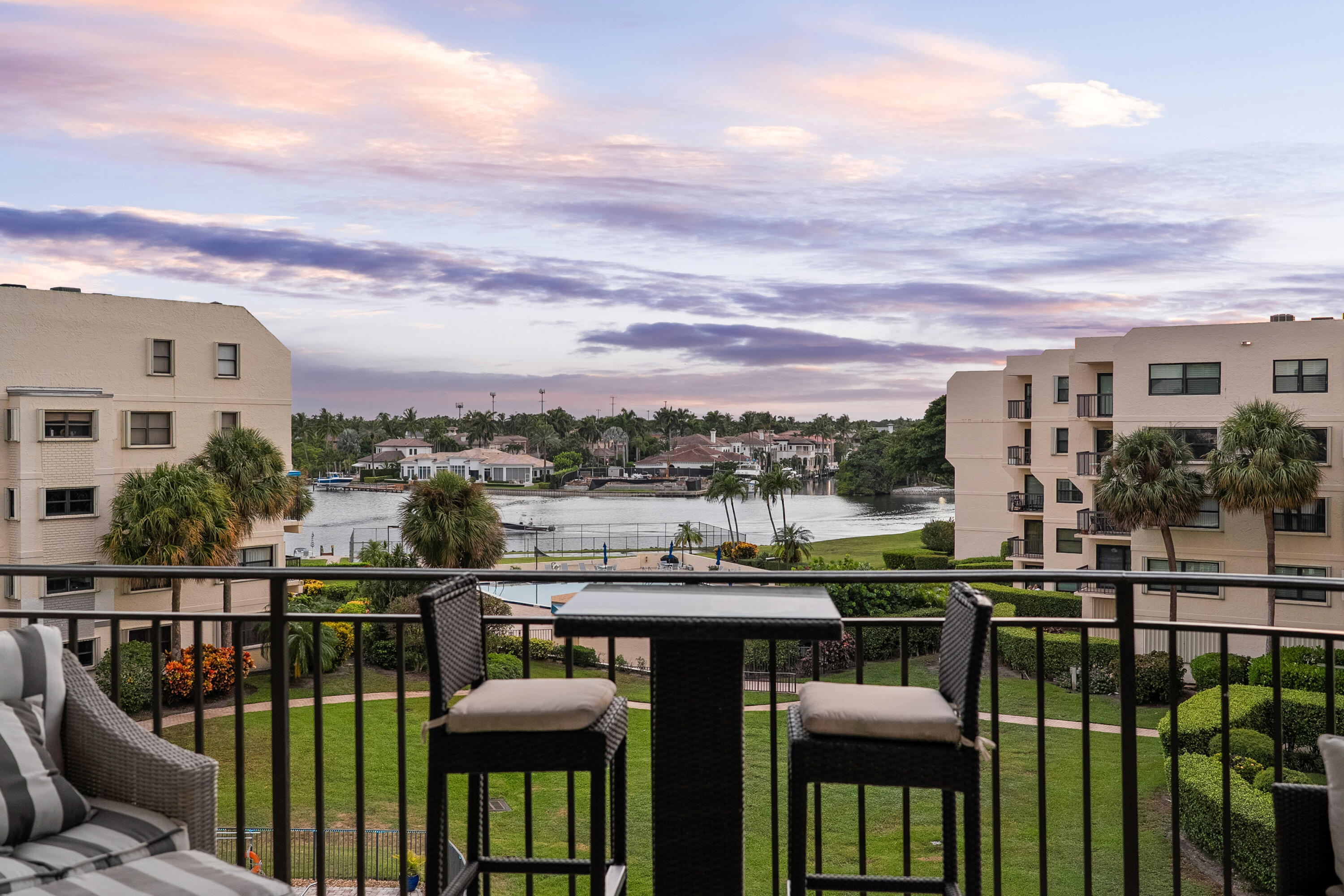 Furnished balcony overlooking a palm-lined waterway at dusk.