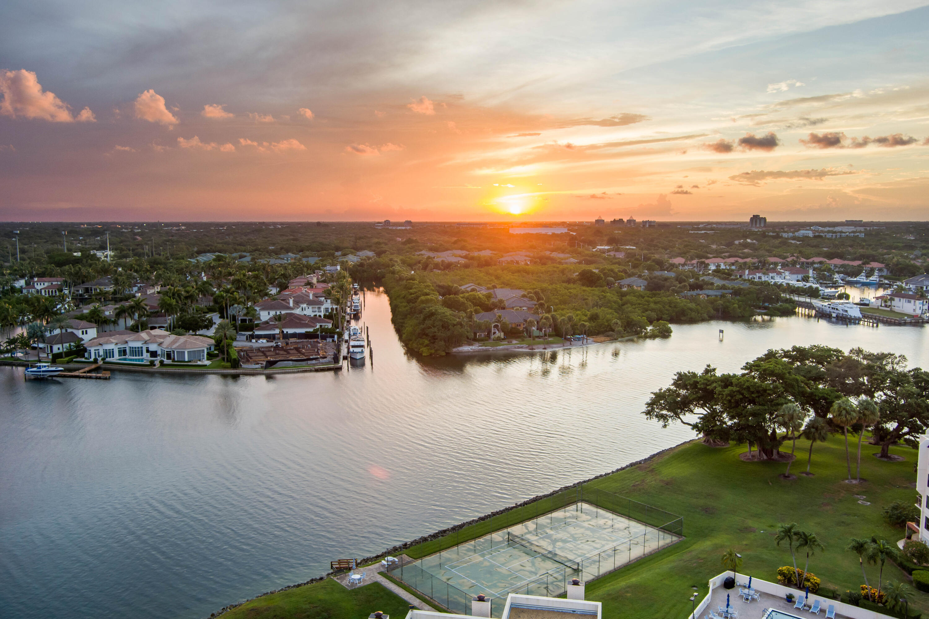 Waterfront community at sunset, with canal-side homes, docks, and a tennis court.