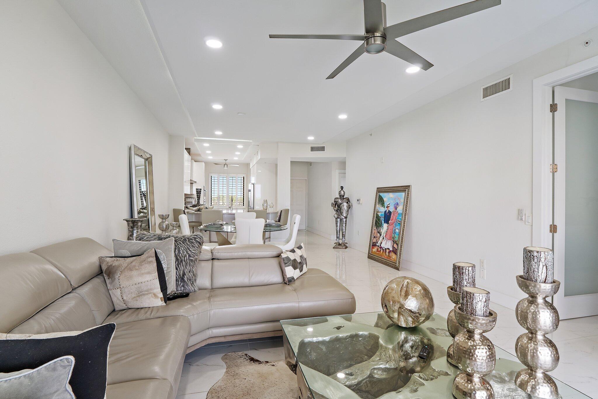 Open-plan living room with a curved gray sectional, glass coffee table, and dining area beyond.