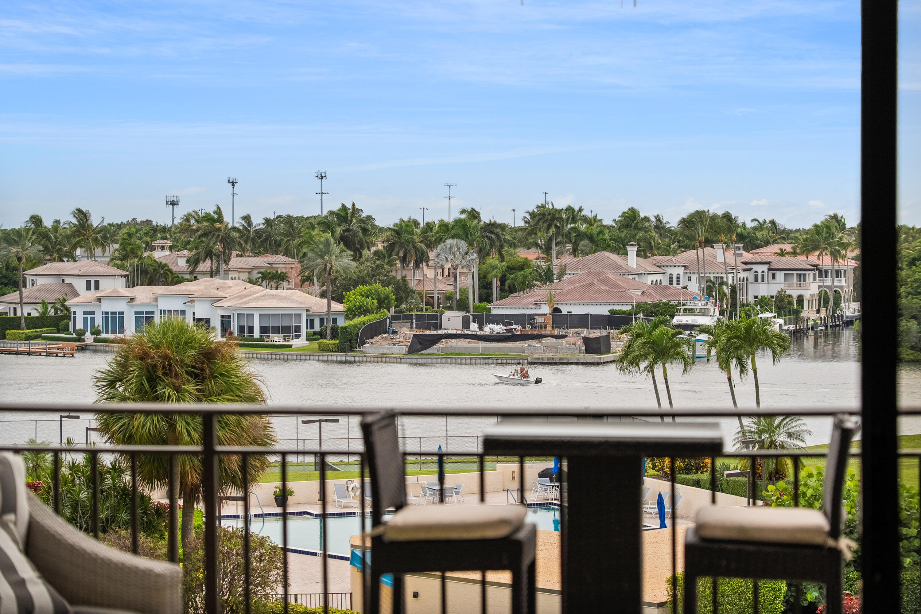 Water view from a furnished balcony, with waterfront homes, a boat, and the community pool below.