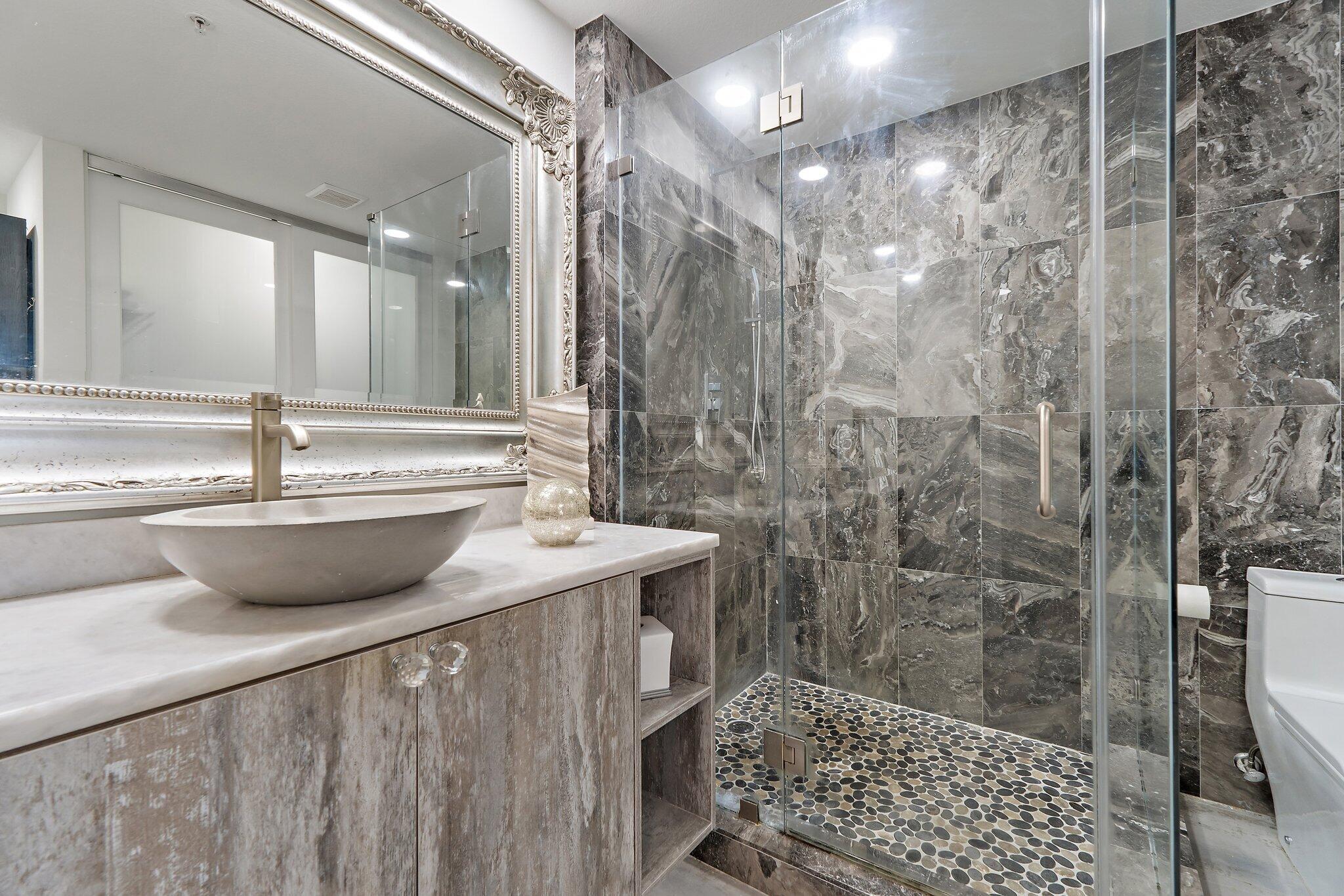 Bathroom with a glass shower, veined stone walls, pebble-tile floor, and vessel sink.