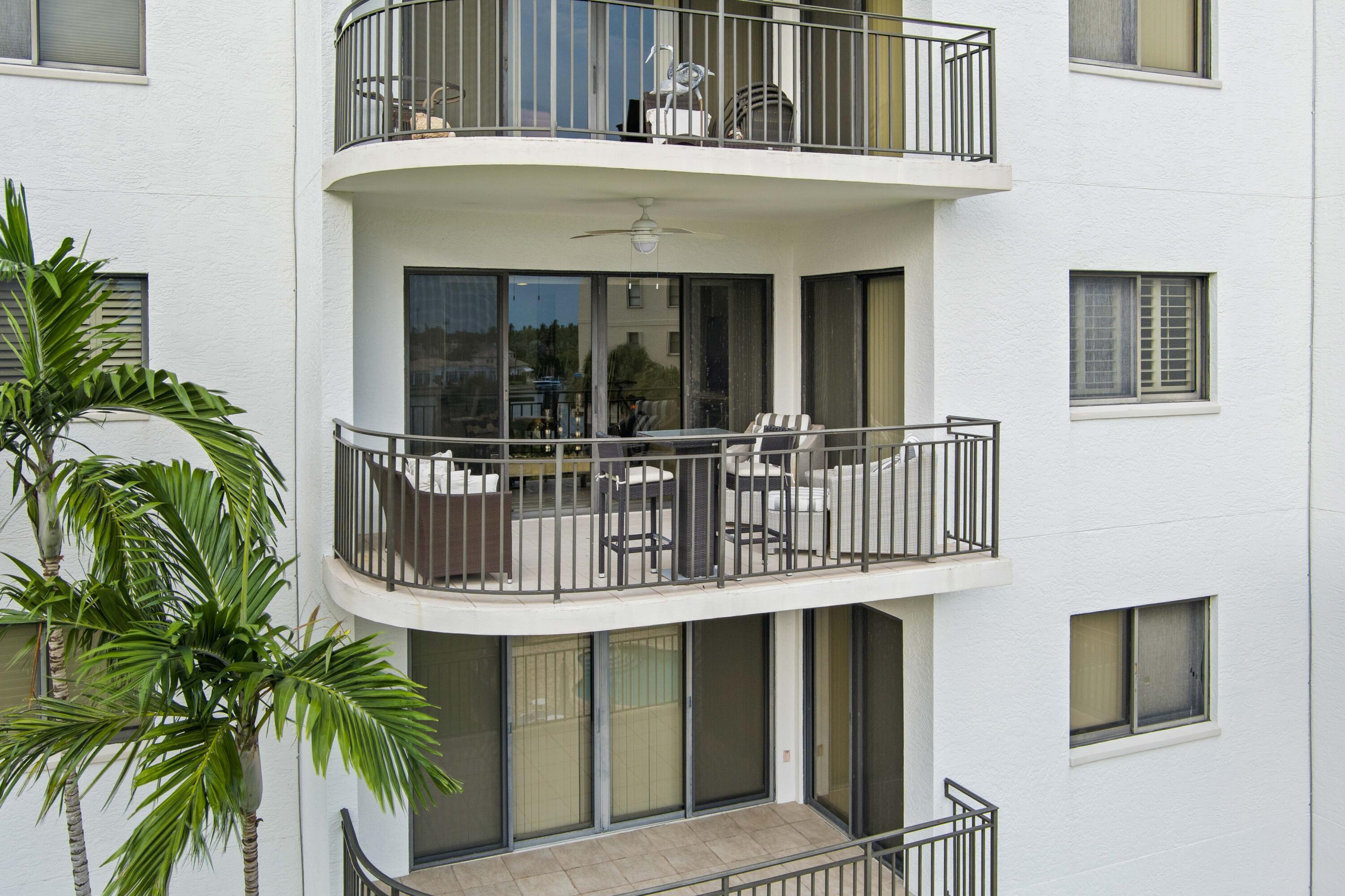 Condominium exterior with curved balconies, patio seating, and palm trees in the foreground.