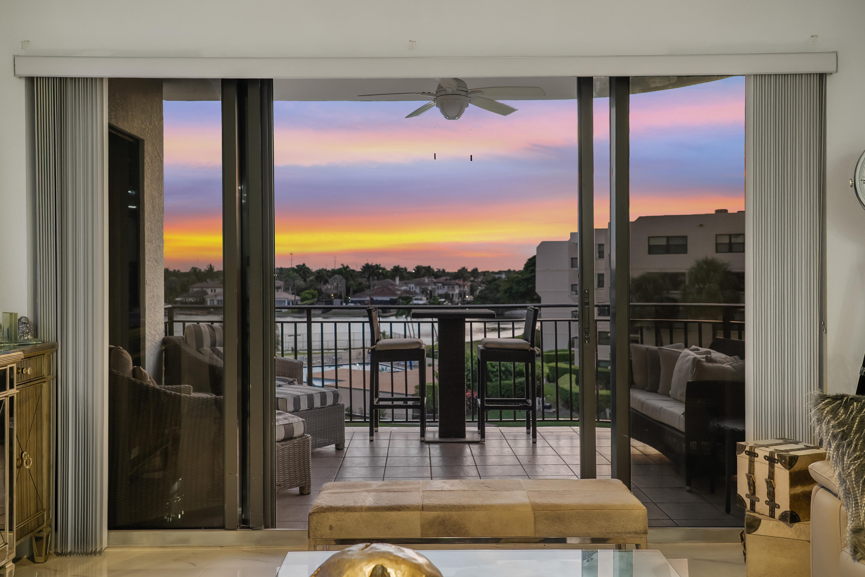 Living room opening onto a furnished balcony overlooking a waterway at sunset.