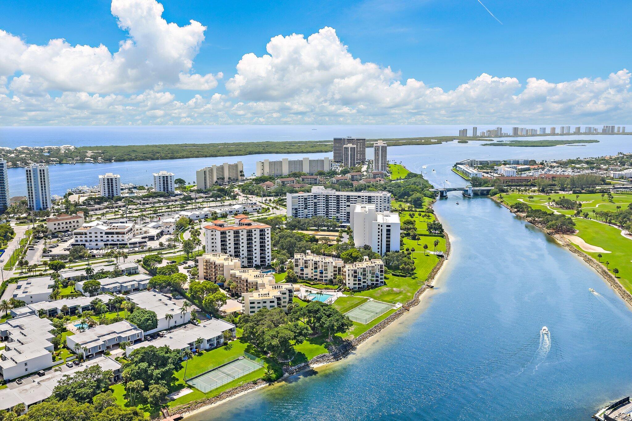 Aerial view of waterfront condominiums, a golf course, and the ocean beyond the waterway.