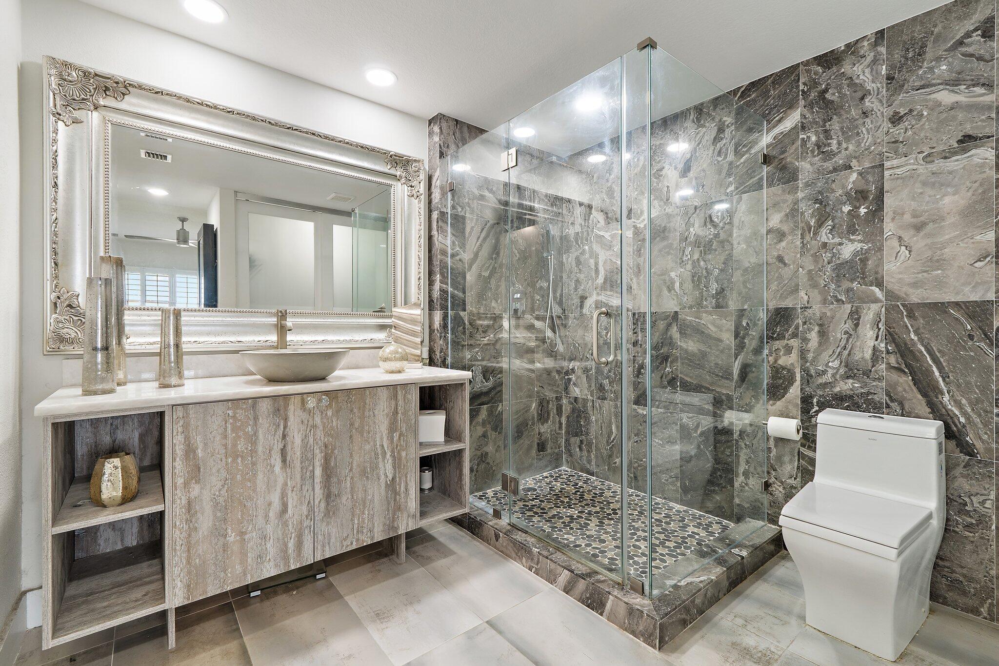 Bathroom with a glass walk-in shower, gray marble walls, pebble floor, and floating vanity.