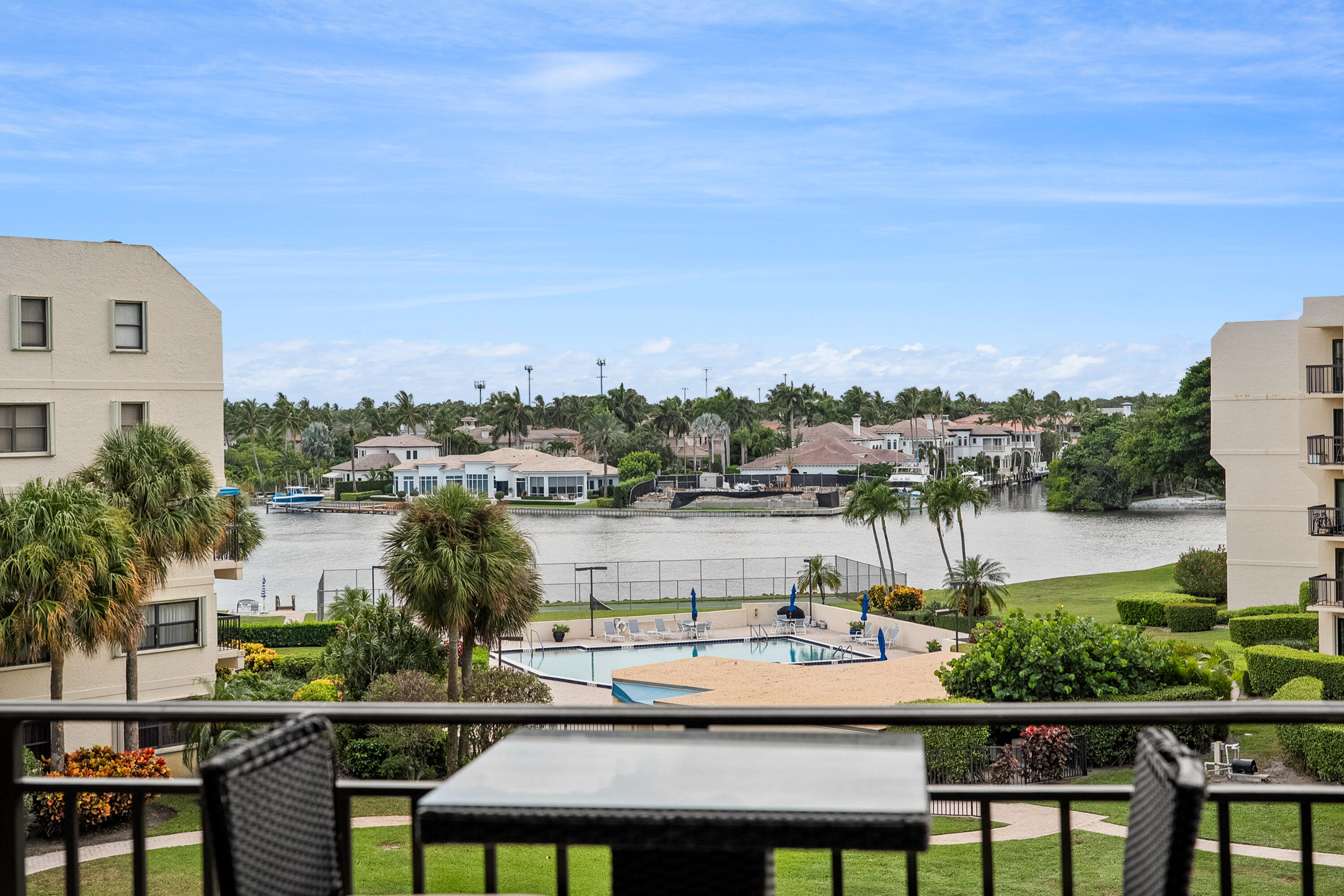 Condo balcony overlooks a palm-lined canal, community pool, and waterfront homes.