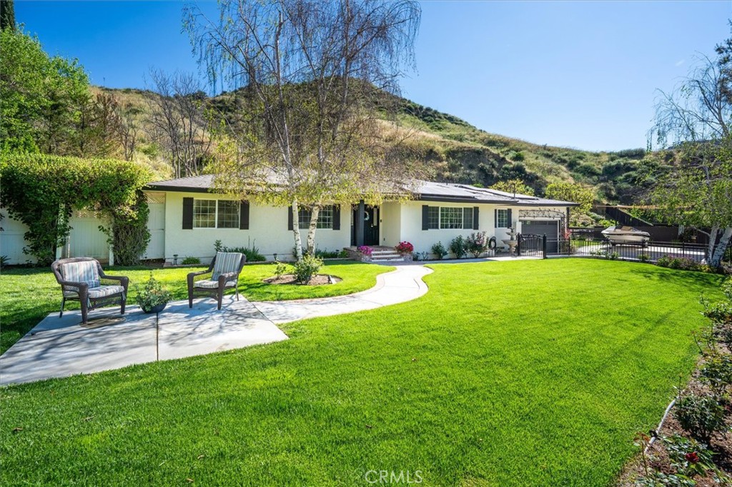 Single-story white home with a curved front walkway, broad lawn, and patio chairs.